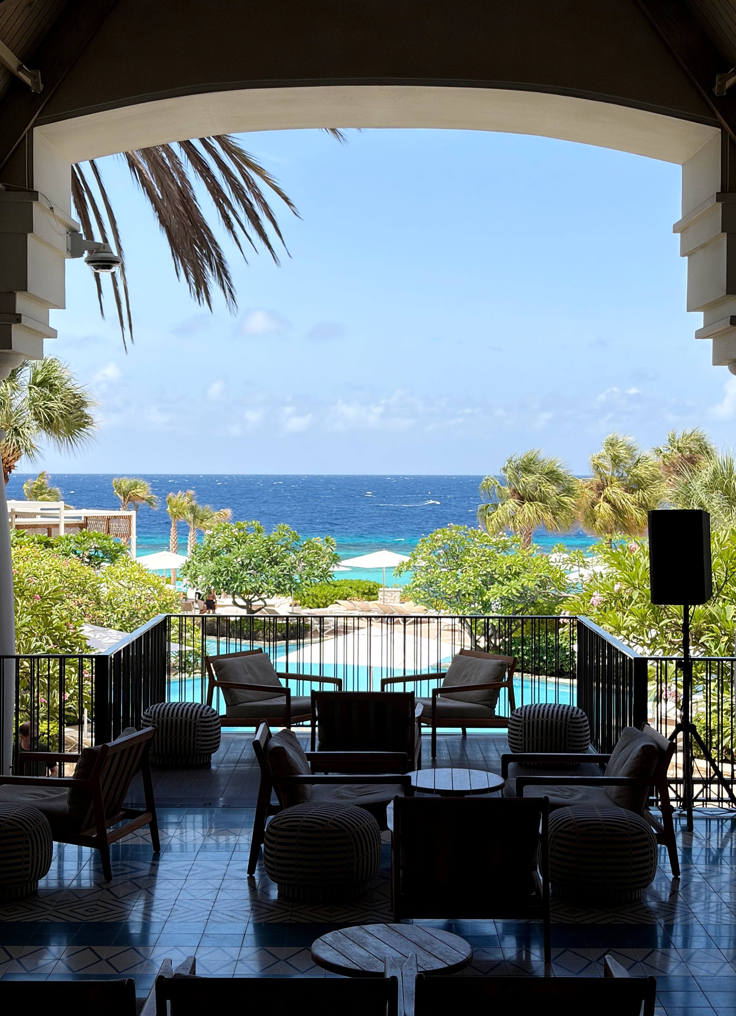 Scenic presumption of an outdoor patio overlooking a lush garden, pool, and water nether a wide sky. Silhouetted chairs and tables successful the foreground