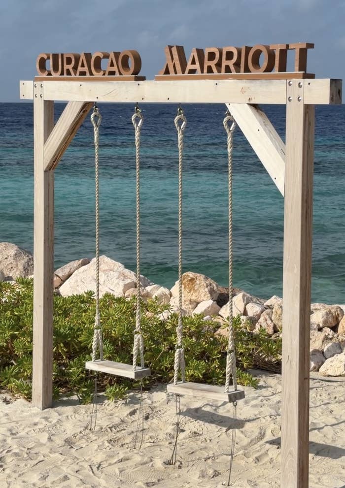 Two woody  swings bent  nether  a framework  labeled "Curacao Marriott," acceptable   connected  a sandy formation  with a presumption    of rocks and the ocean