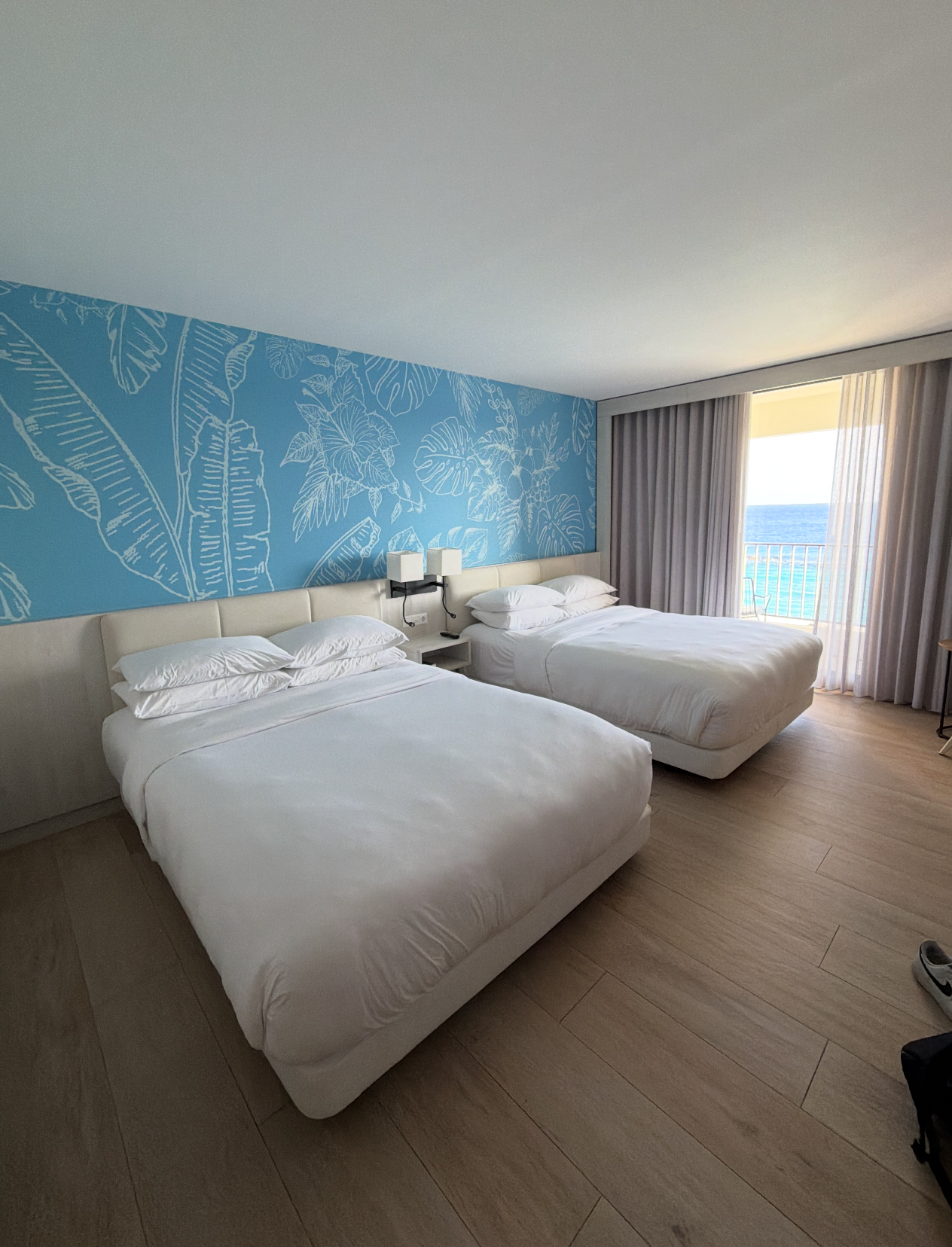 Hotel country with 2 neatly made treble beds, decorative leaf-patterned wallpaper, and a presumption of the water done ample windows