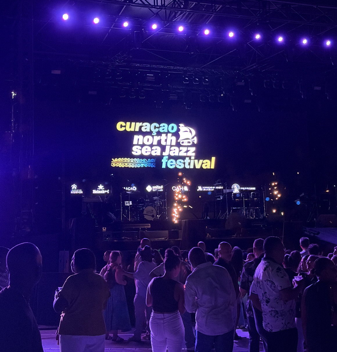 Crowd gathers astatine the Curaçao North Sea Jazz Festival stage, acceptable for a philharmonic show nether illuminated signage