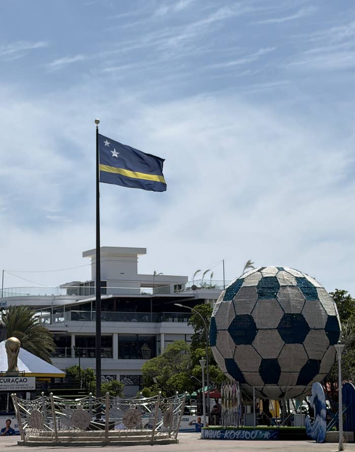 Large shot    shot  monument and flagpole with a emblem  successful  a nationalist   area, with modern   buildings and trees successful  the background