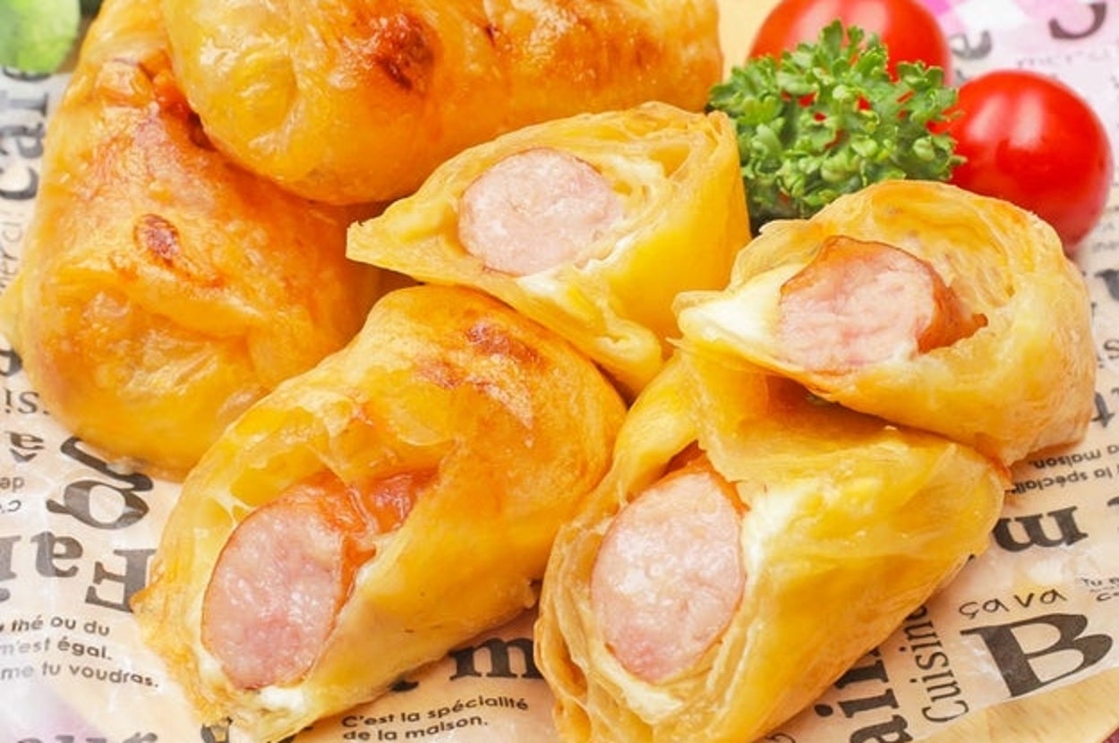 ライスペーパーでウインナーとチーズを包んで焼いたパイ。木の皿に盛り付けられている。
