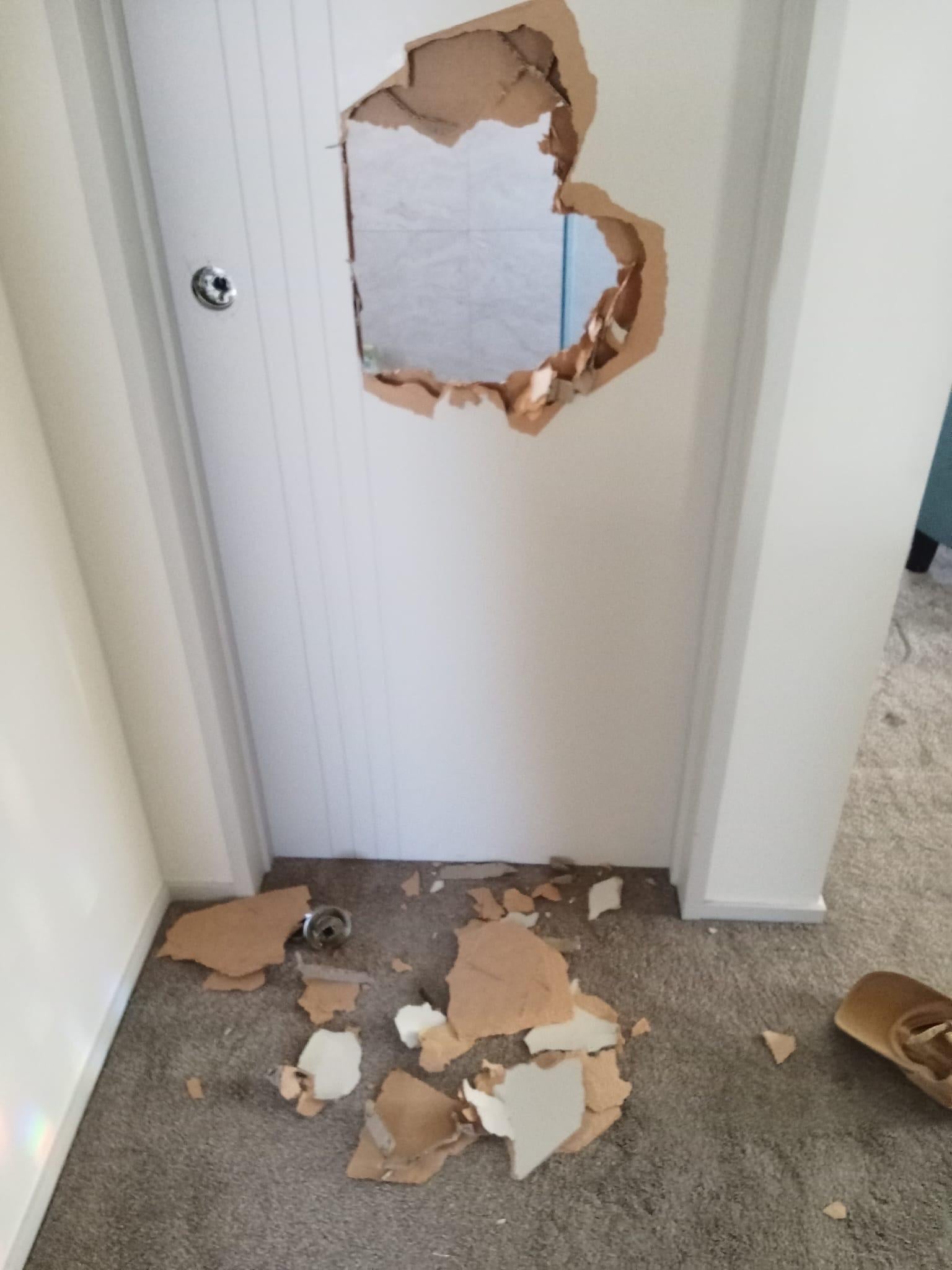 Door with a large hole punched through, surrounded by debris on the floor
