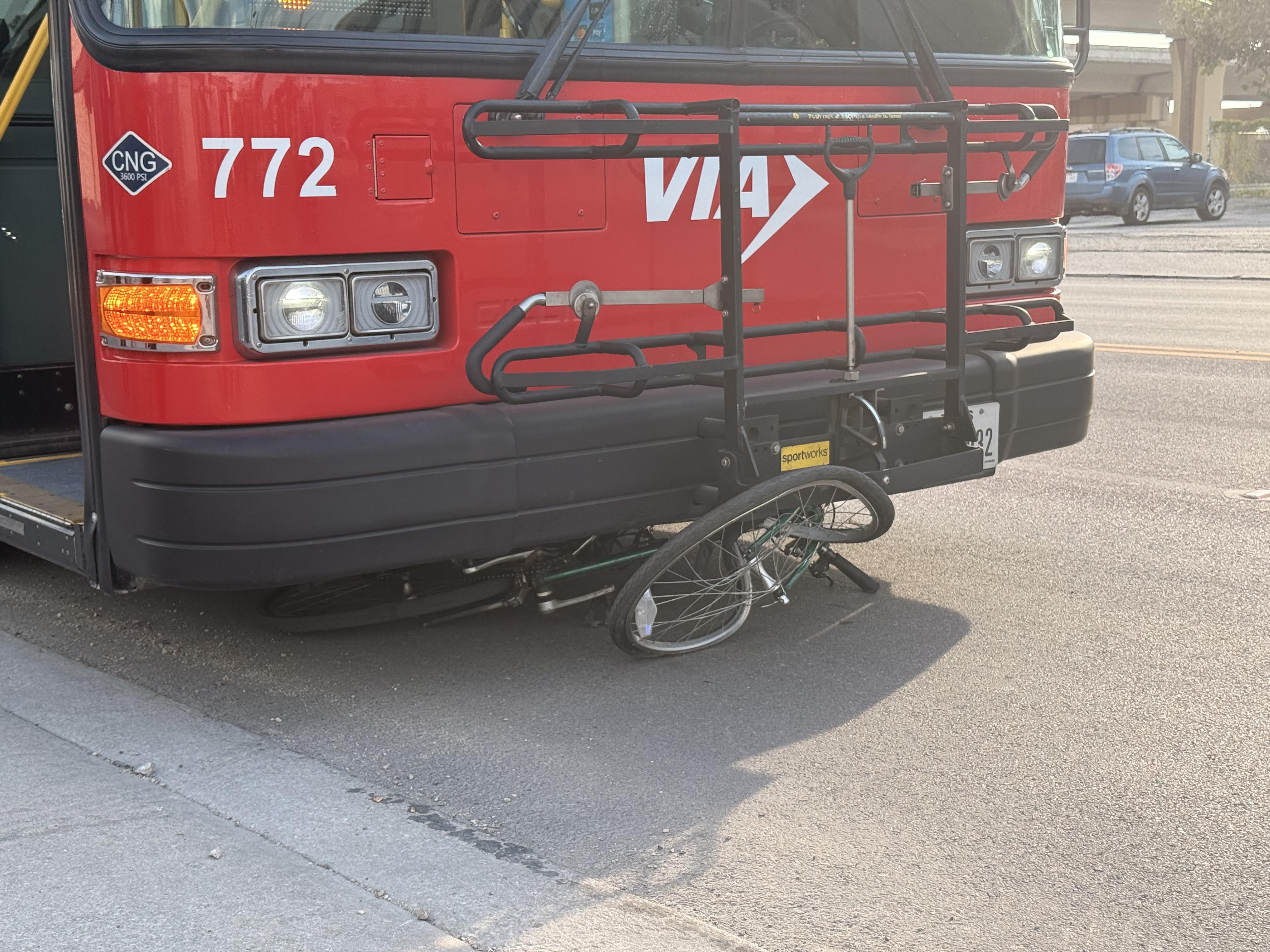 City bus collided with a bicycle, with the bike trapped under the front bumper on a road. No people are visible