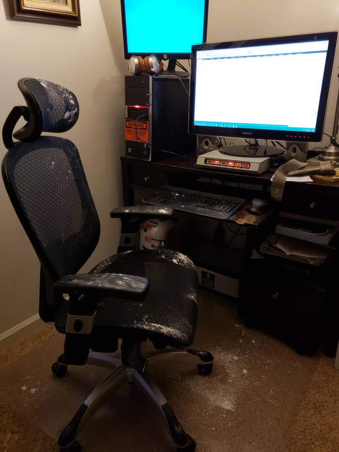 Office chair and desk covered in spilled powder, with computer monitors and equipment nearby