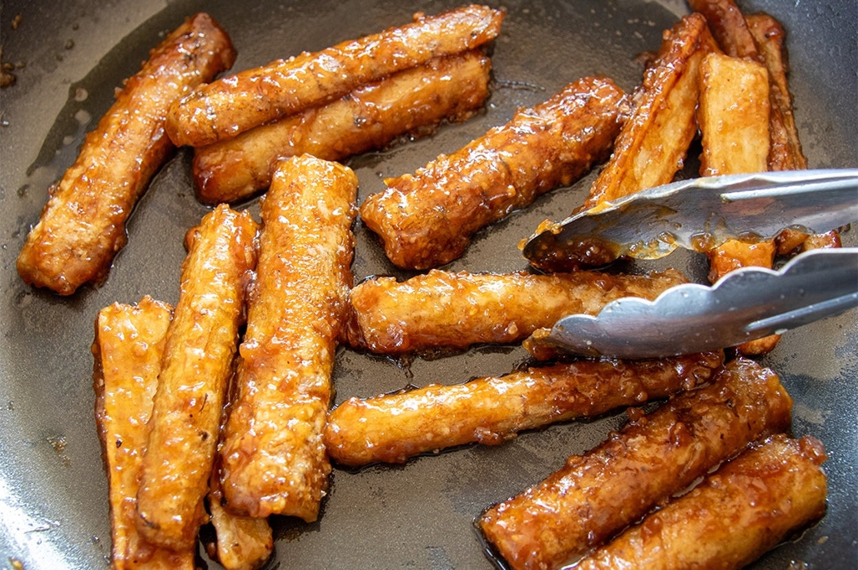 フライパンで焼かれた焼肉のたれがかかったごぼうがトングで調理されている。