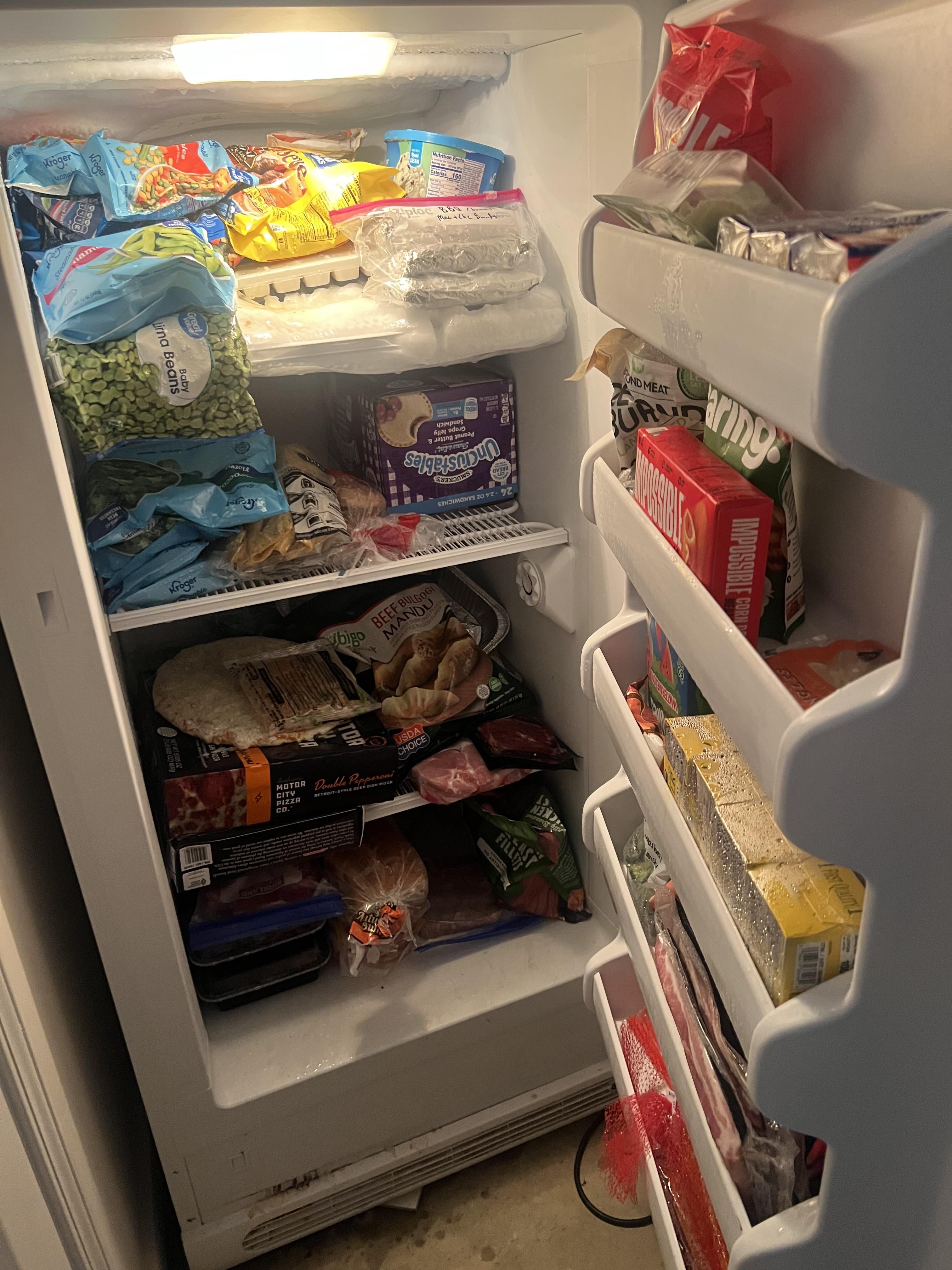 A packed freezer with various frozen foods, including vegetables, ice cream, and frozen meals stored on shelves and in the door compartments