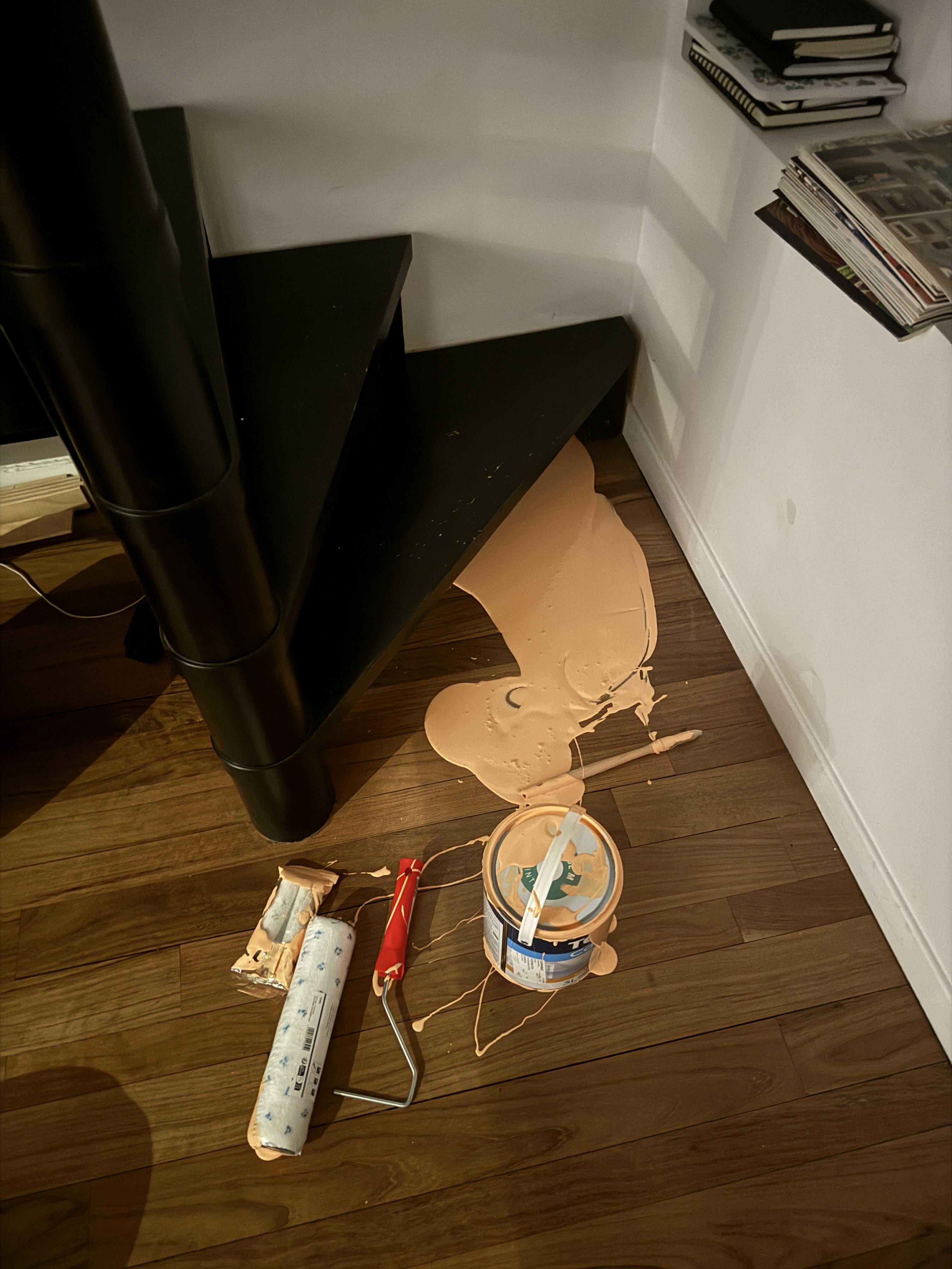 Spilled paint can and rollers on wooden floor near black stairs