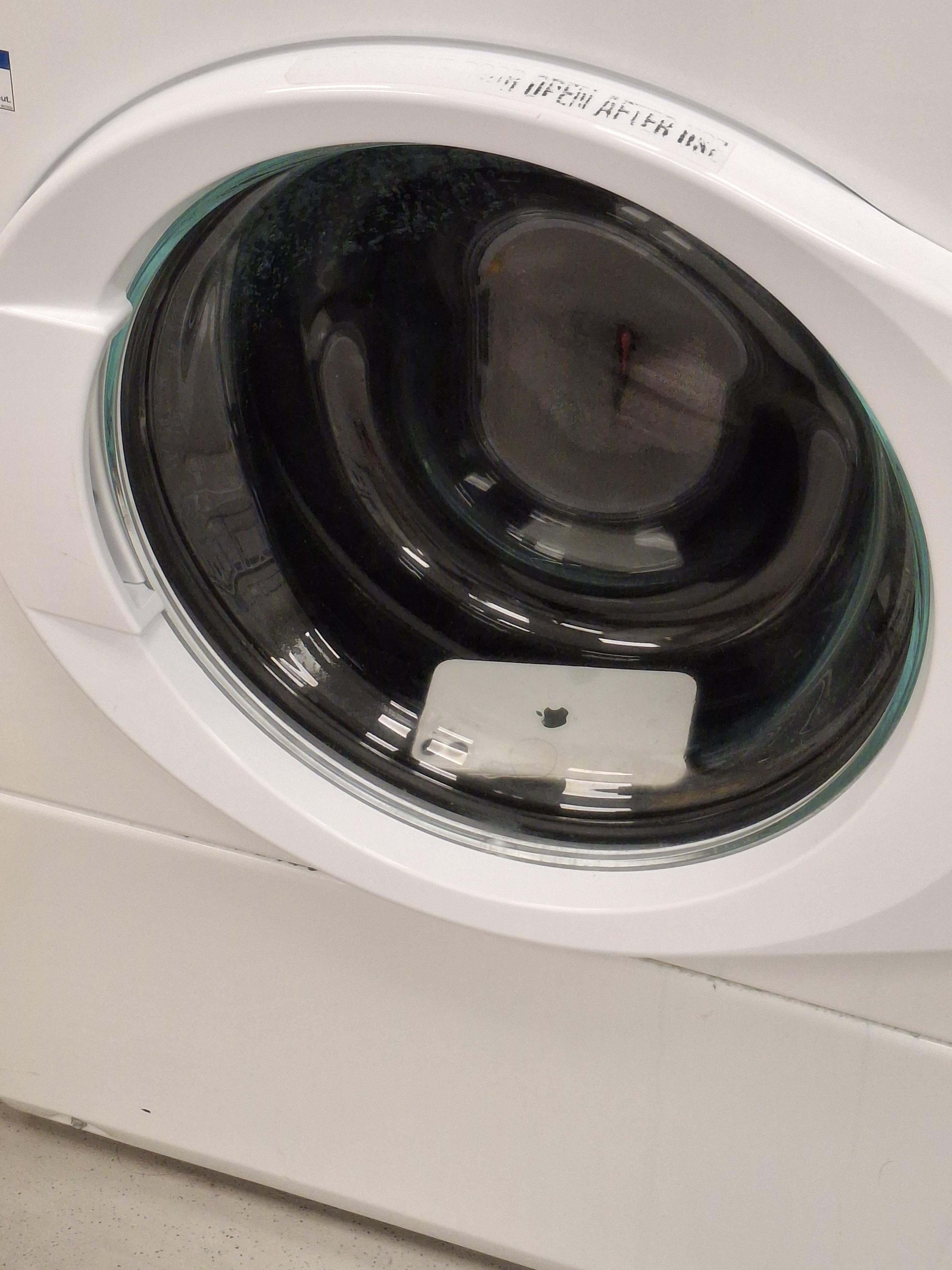 A smartphone is inside the drum of a washing machine, seen through the glass door