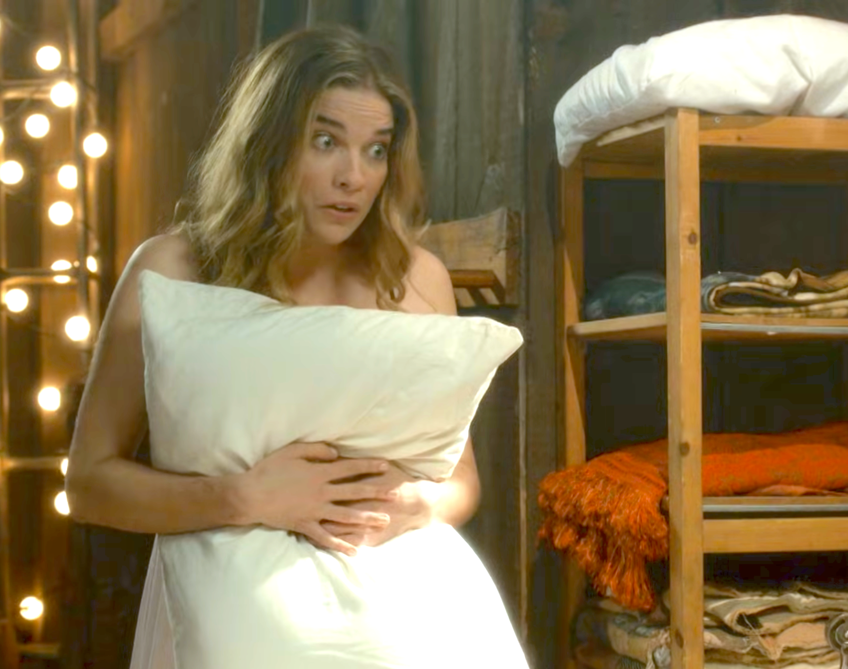 Person holding a pillow to their chest, looking amazed  successful  a cozy country   with blankets connected  shelves