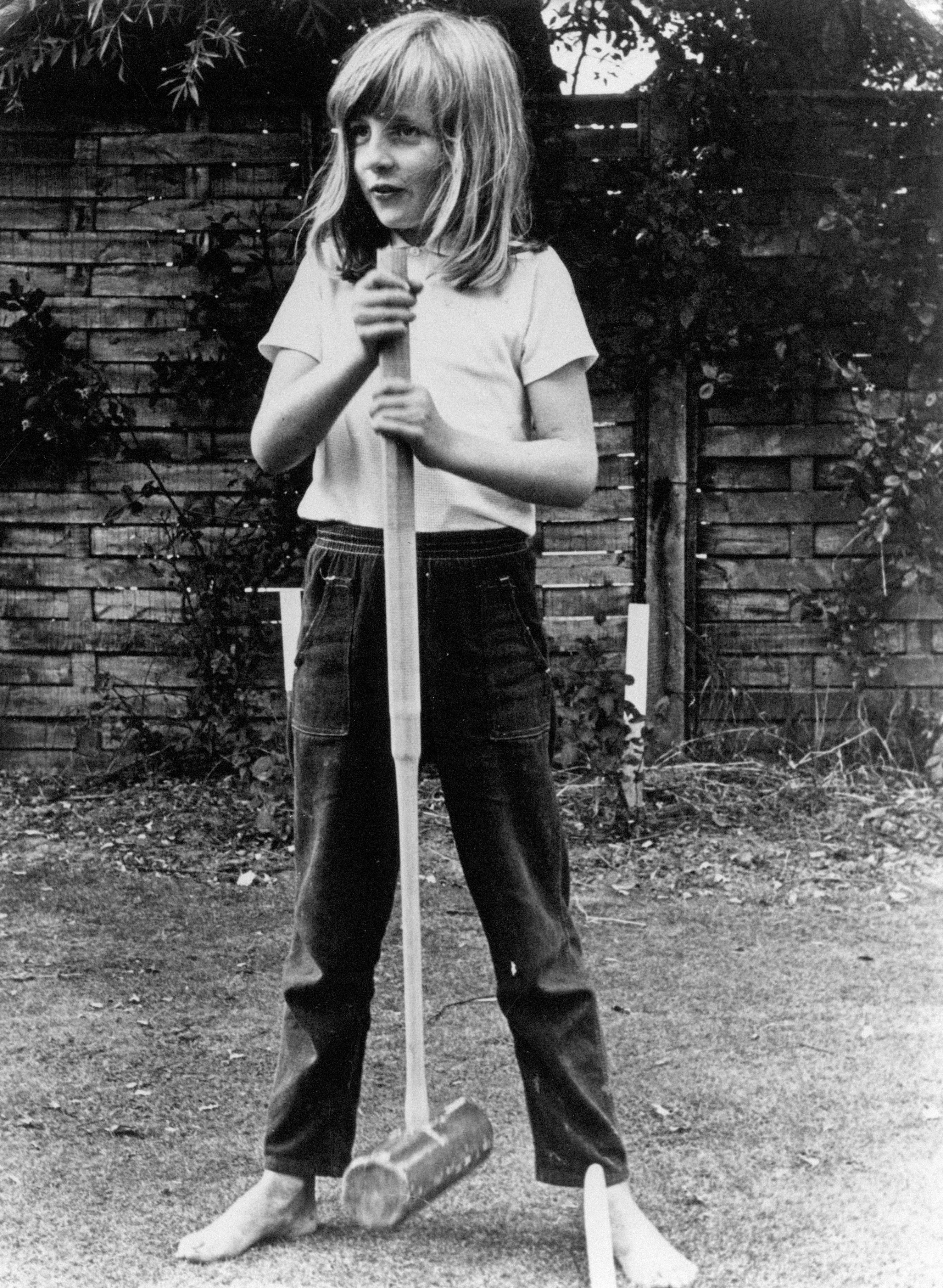 Lady Diana Spencer wearing casual clothing stands barefoot while holding a croquet mallet
