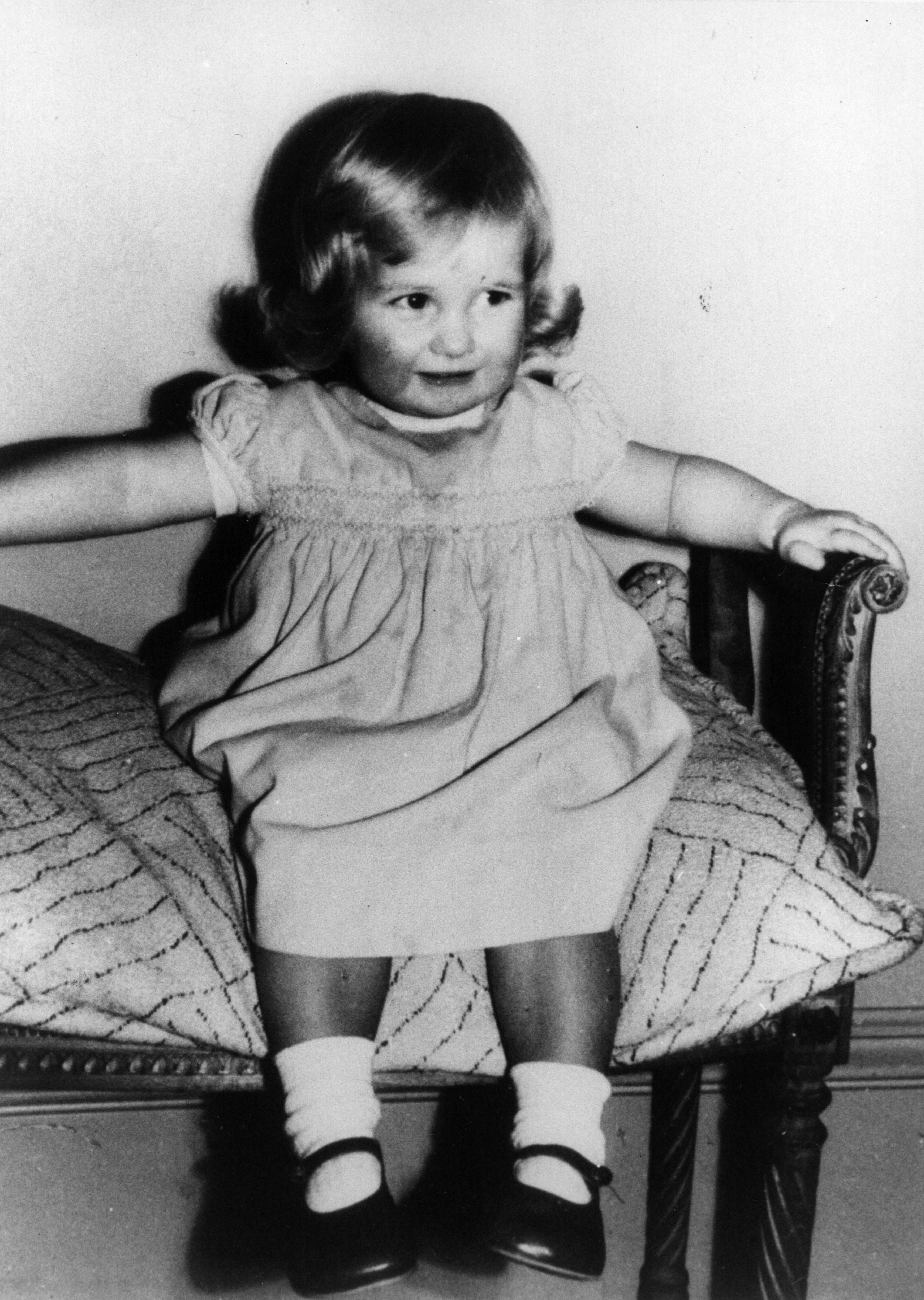 Lady Diana Spencer sits on a chair, wearing a dress and socks with strap shoes, looking to the side