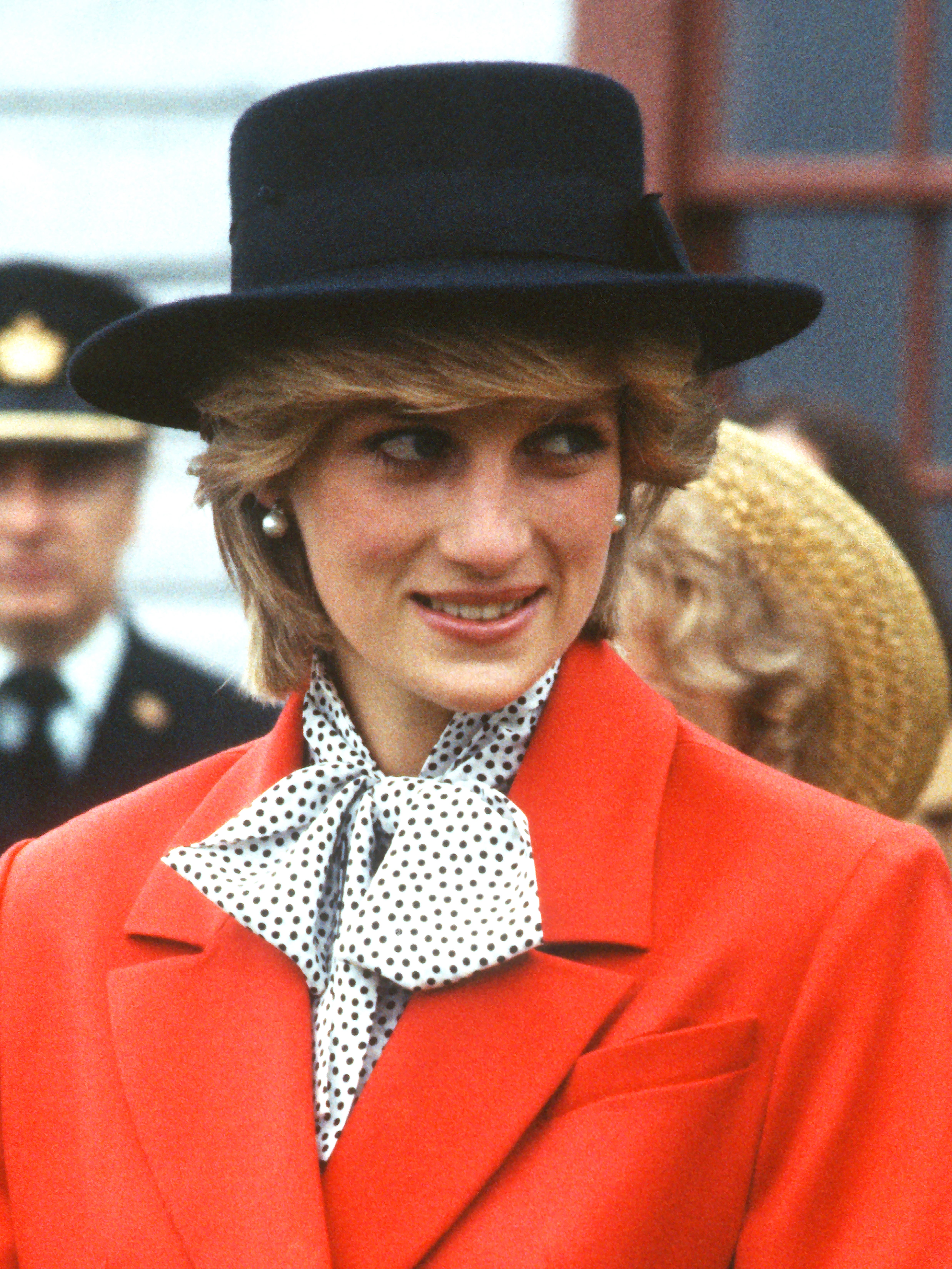 Princess Diana wearing a polka dot blouse, red blazer, and black hat in 1983
