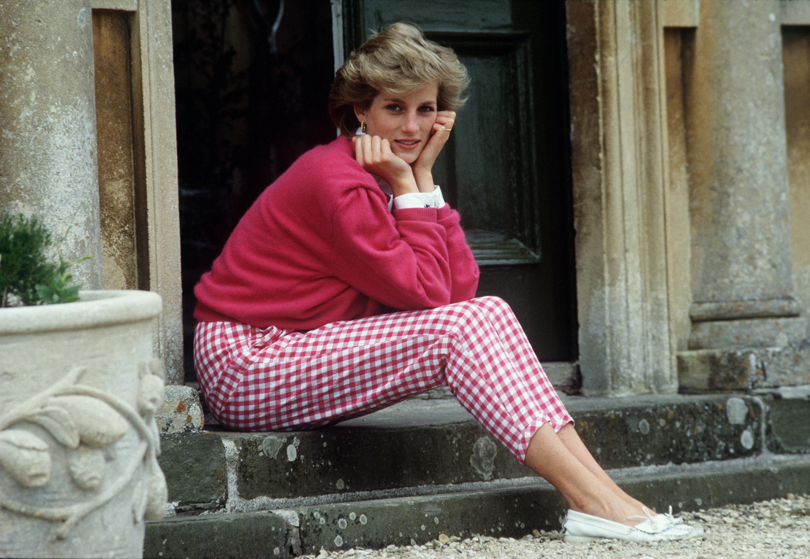 Person seated on steps, wearing a casual outfit with a top and checkered pants, embodying a relaxed, elegant style