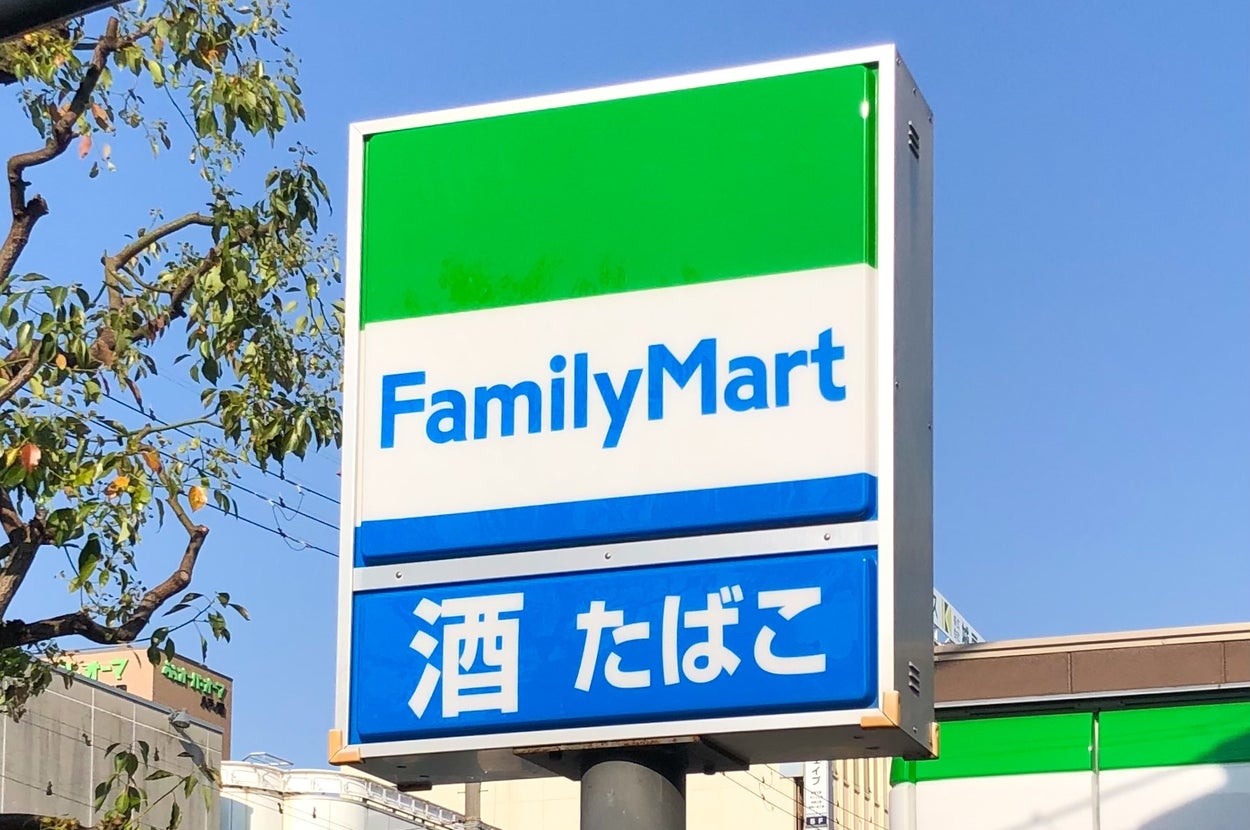 ファミリーマートの看板。下には「酒」「たばこ」と表示されている。周囲に木が見える。