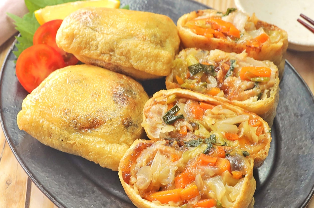 お皿に盛られた野菜と肉が詰まった揚げ豆腐の包み料理。添え物にレモンとトマト。