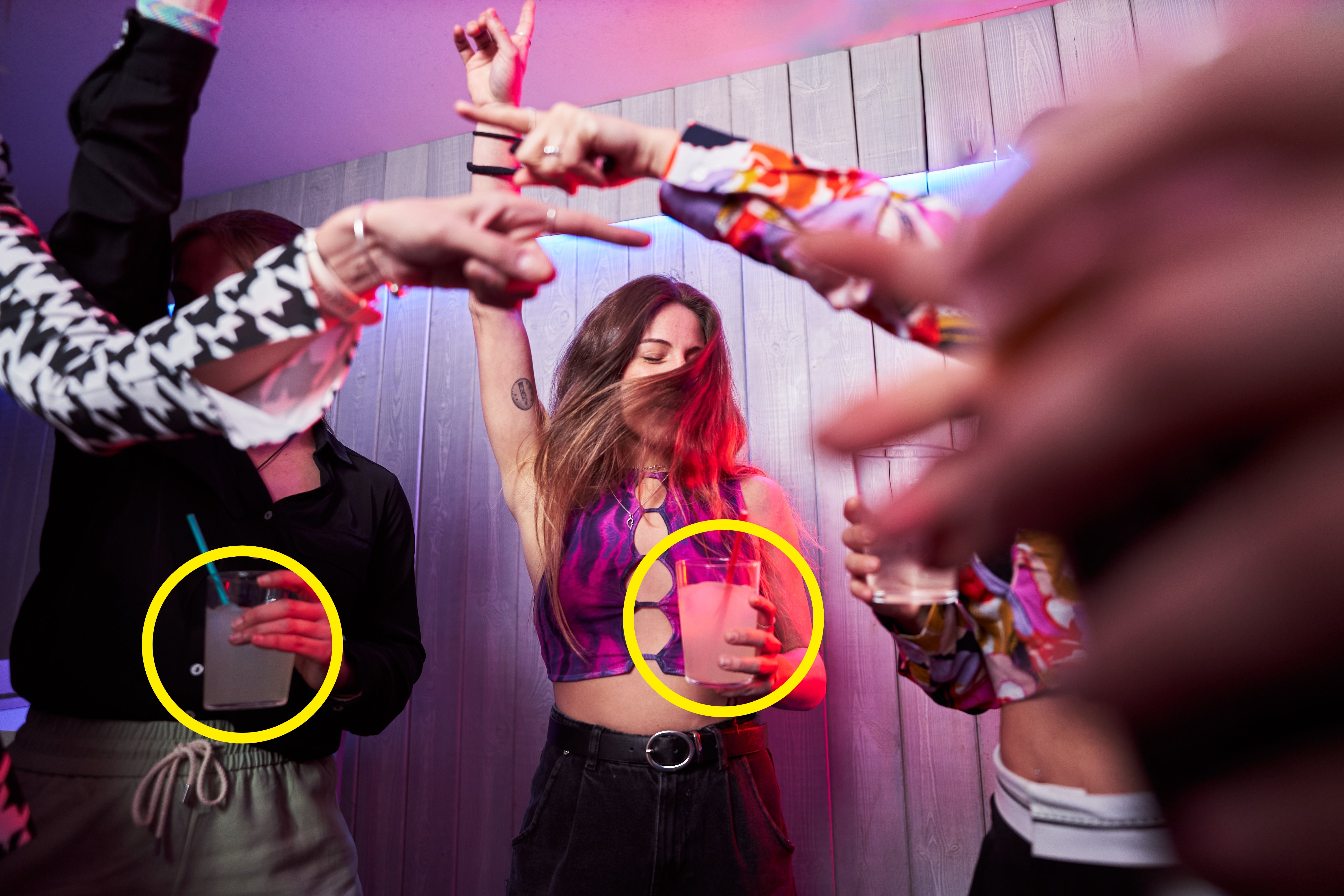People dancing at a lively party, holding drinks, with one person in a stylish cut-out top as the focus