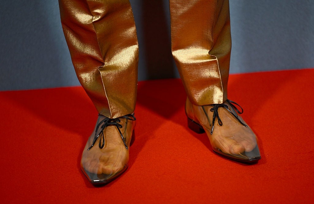 Person wearing shiny pants and clear shoes with socks on a red carpet