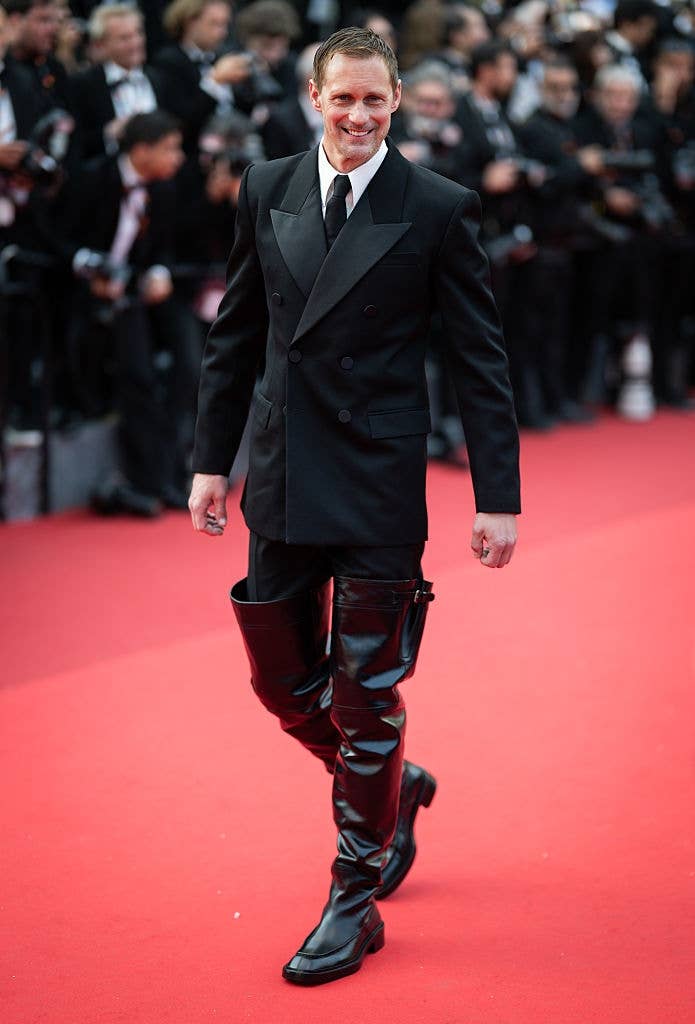Man in double-breasted suit with unique, high black boots walks confidently on red carpet