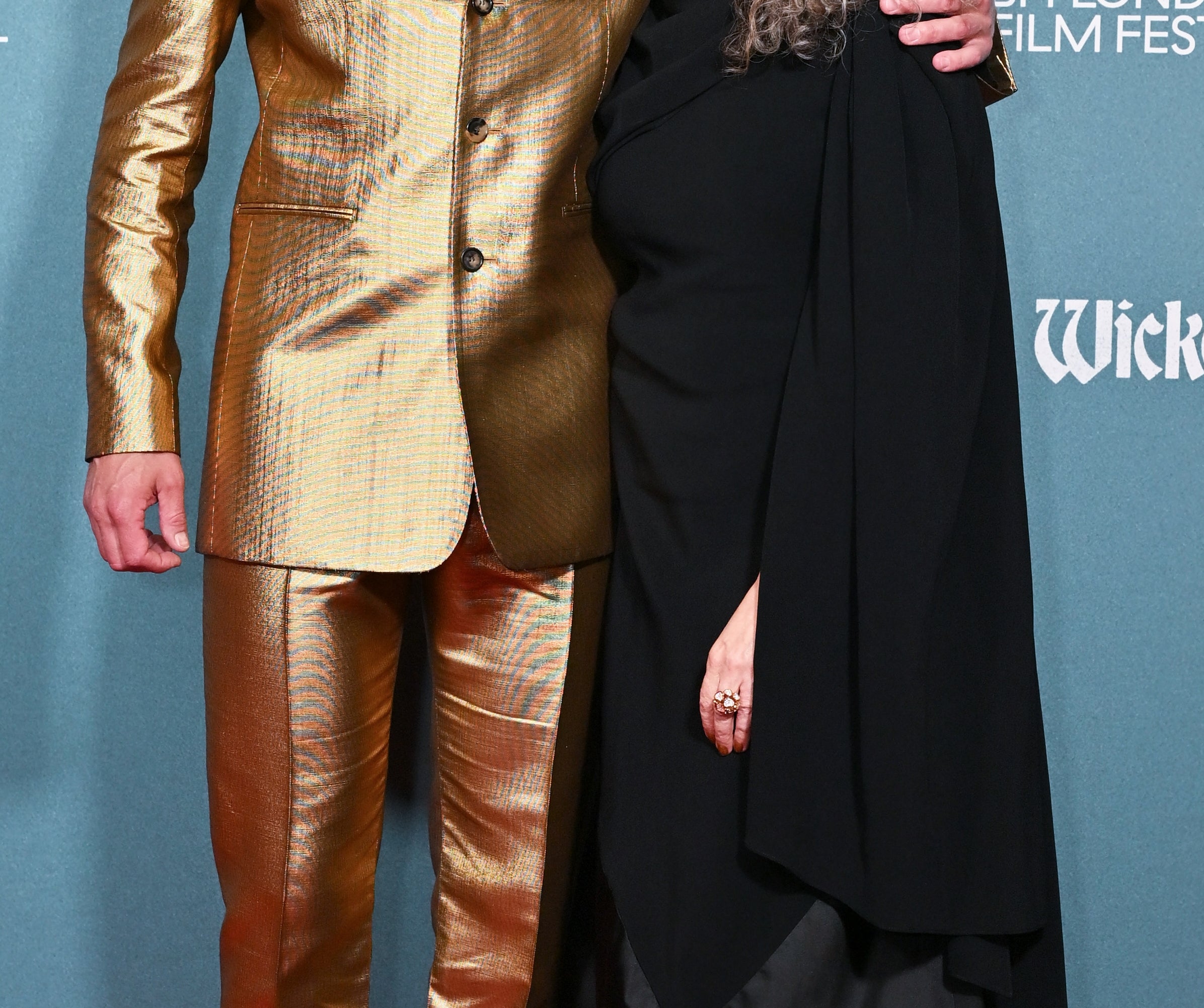 Two people pose on the red carpet; one in a gold suit, the other in a black dress and cape, at the BFI London Film Festival