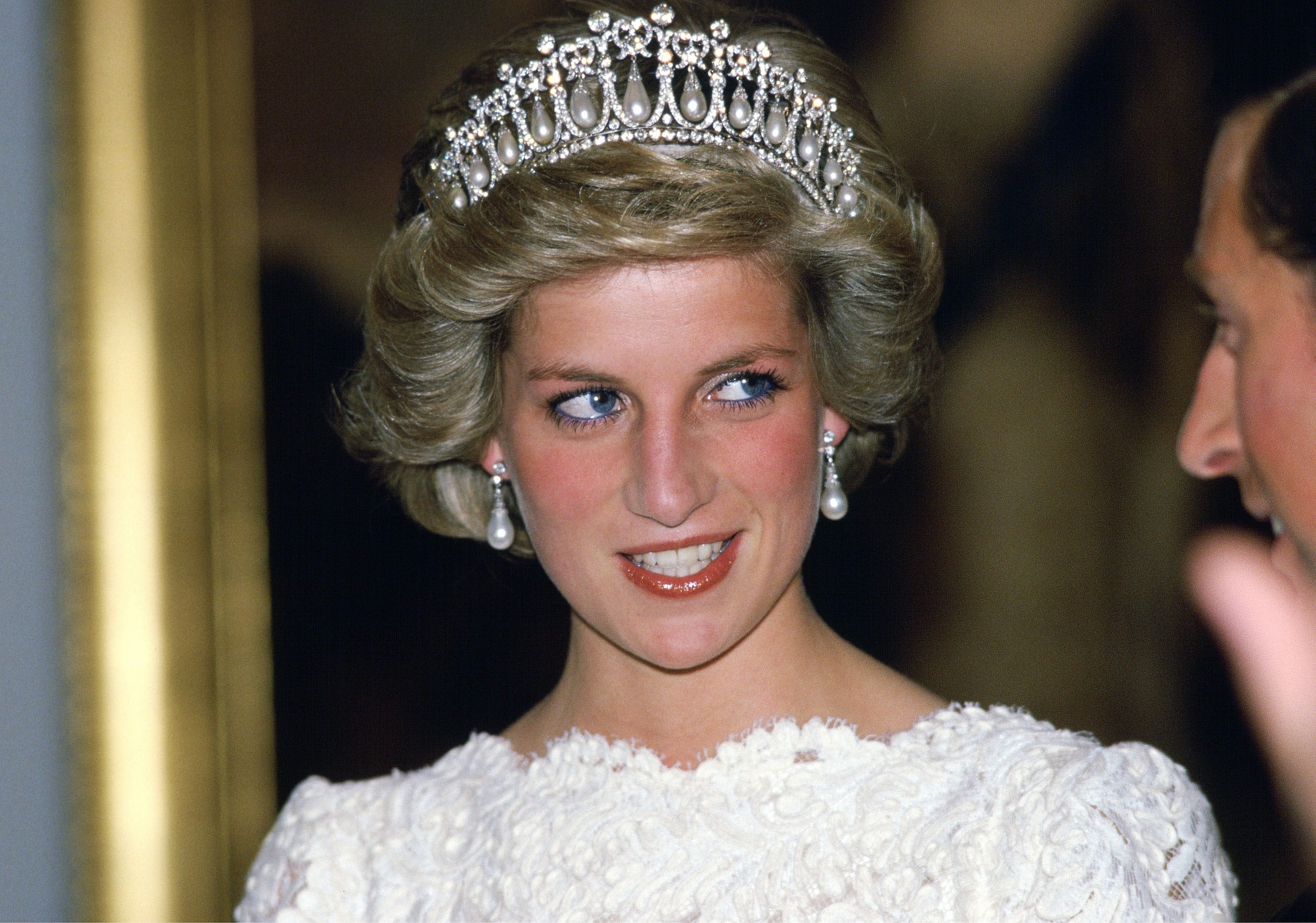 Princess Diana wearing pearl earrings, a tiara, and a white outfit