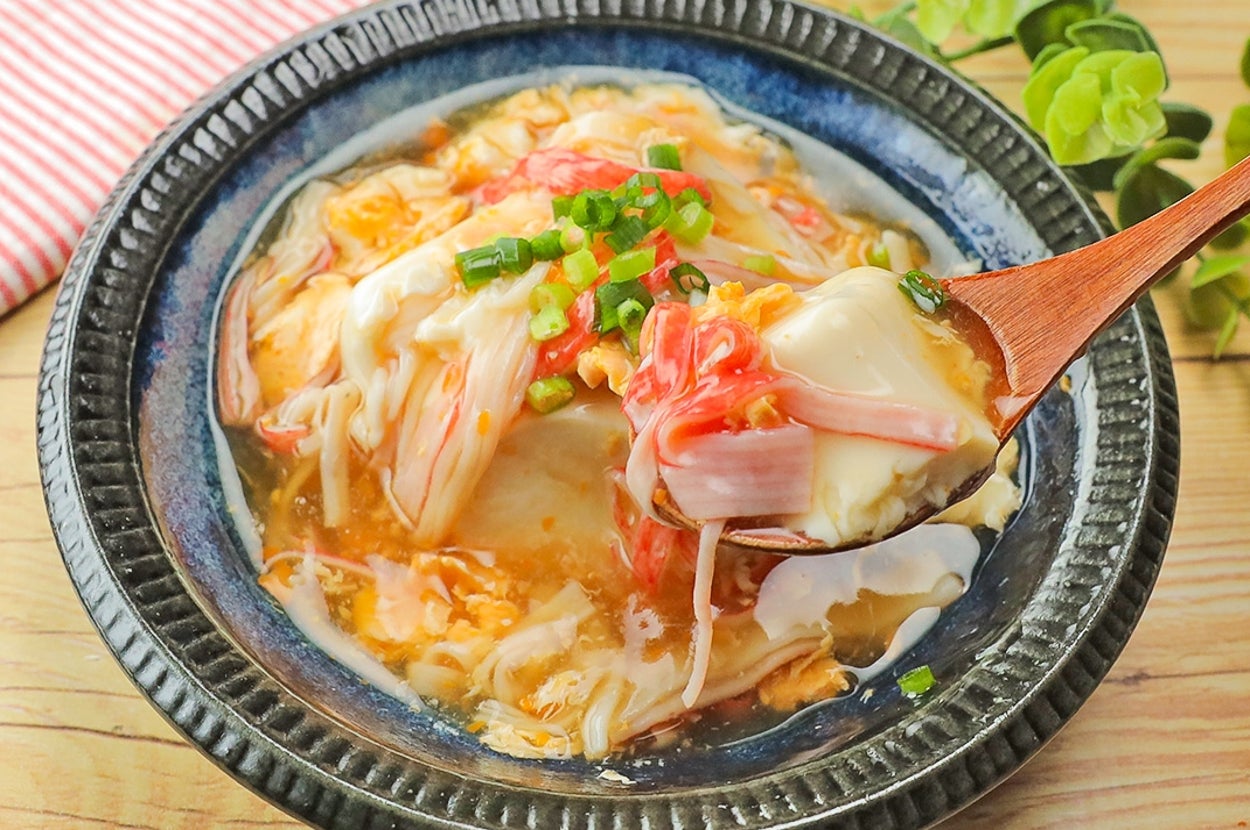 皿に盛られた中華風豆腐料理。カニカマ、ネギがのせられ、美味しそうな様子。木製のスプーンが添えられている。