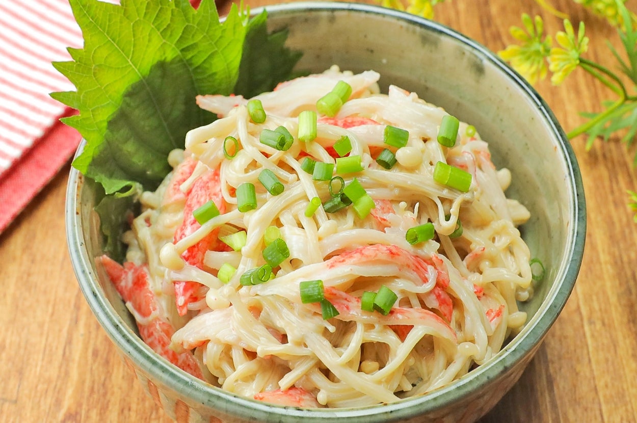 カニカマと葱をトッピングしたパスタサラダが、シソの葉とともに器に盛られている。背景に赤の布。