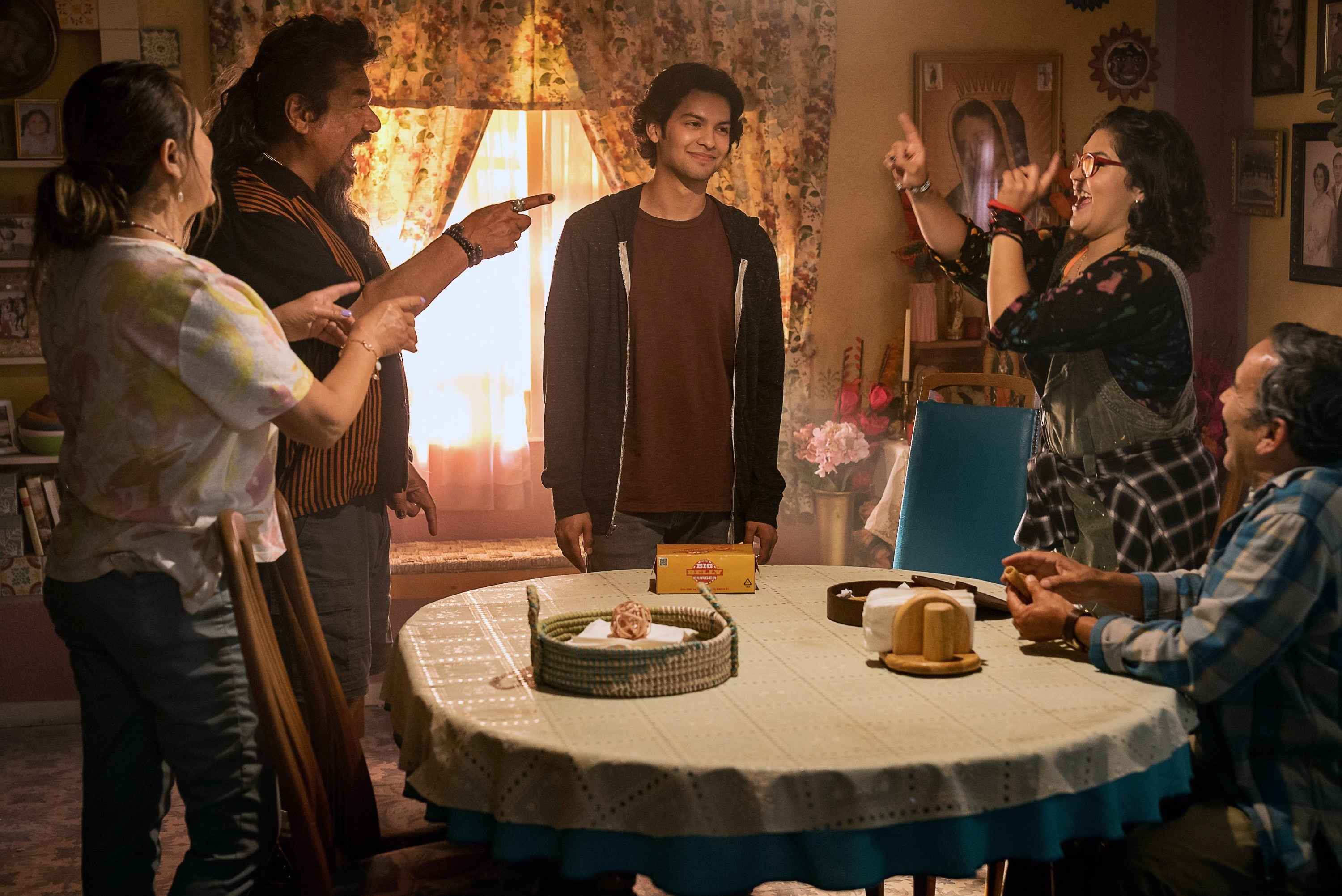 Five people are gathered around a table, smiling and engaging with one another in a cozy, lived-in room