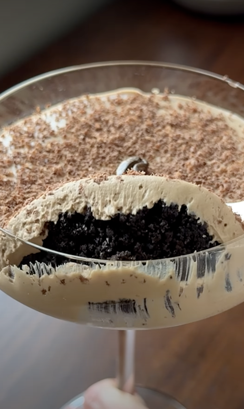 Glass with layered cocoa  dessert, topped with grated cocoa  and cream