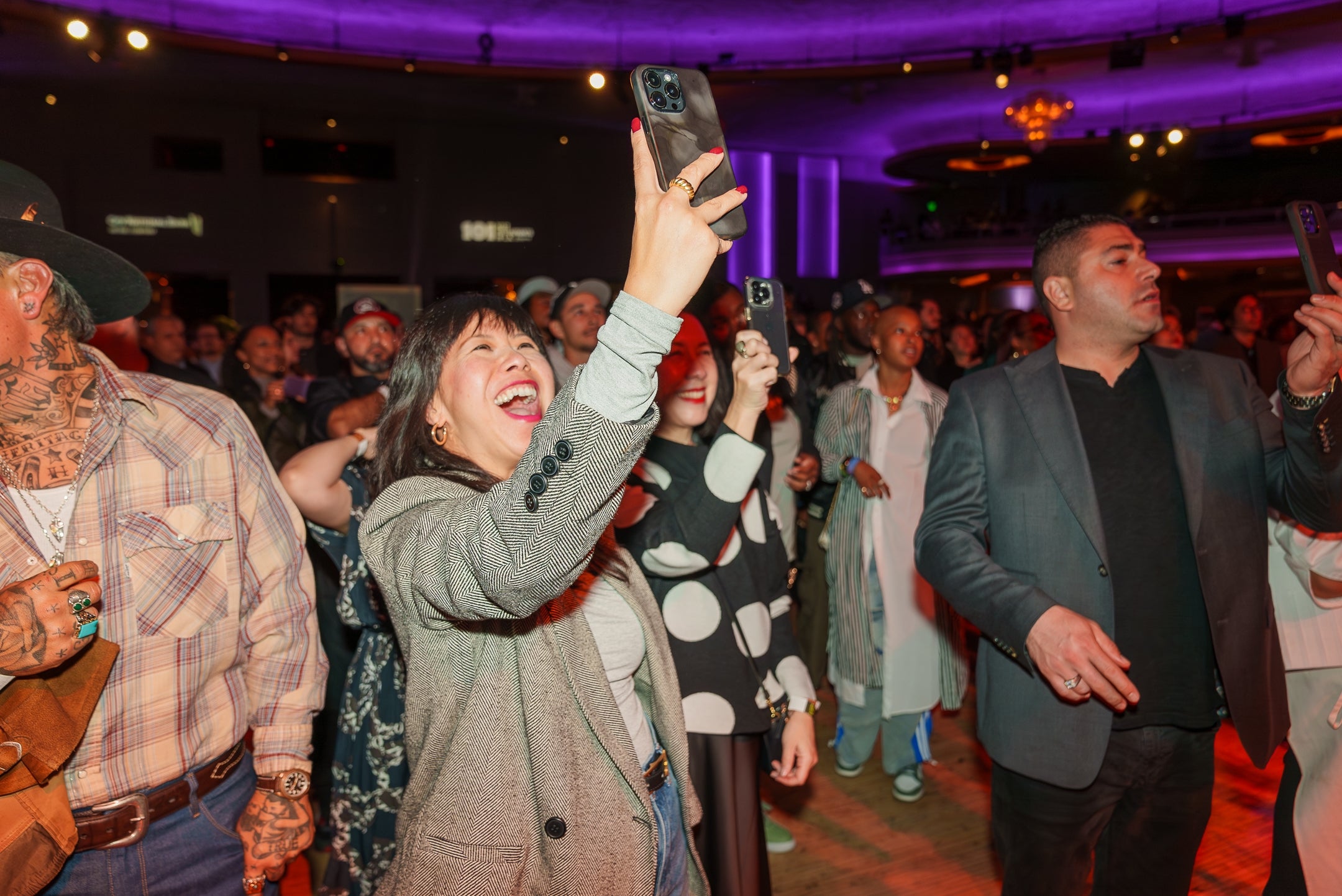 People astatine  an event, smiling and taking photos with phones successful  a lively atmosphere