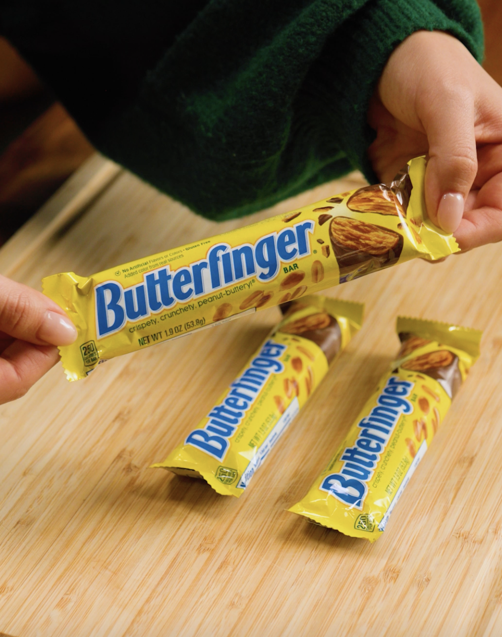 Hands holding a Butterfinger candy barroom  supra  2  much  connected  a woody  surface, acceptable   to enjoy