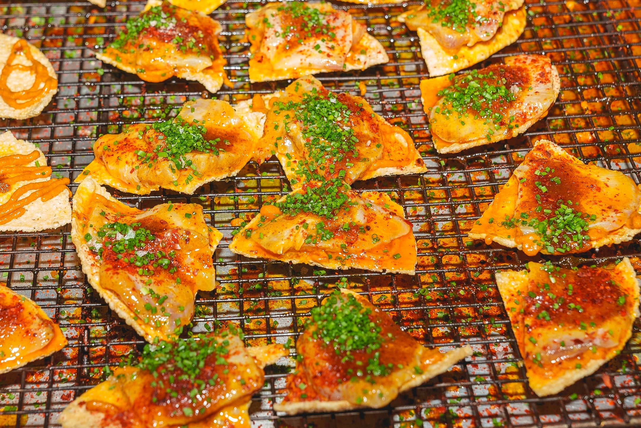 Crispy chips topped with melted cheese, sprinkled with herbs and spices connected  a cooling rack