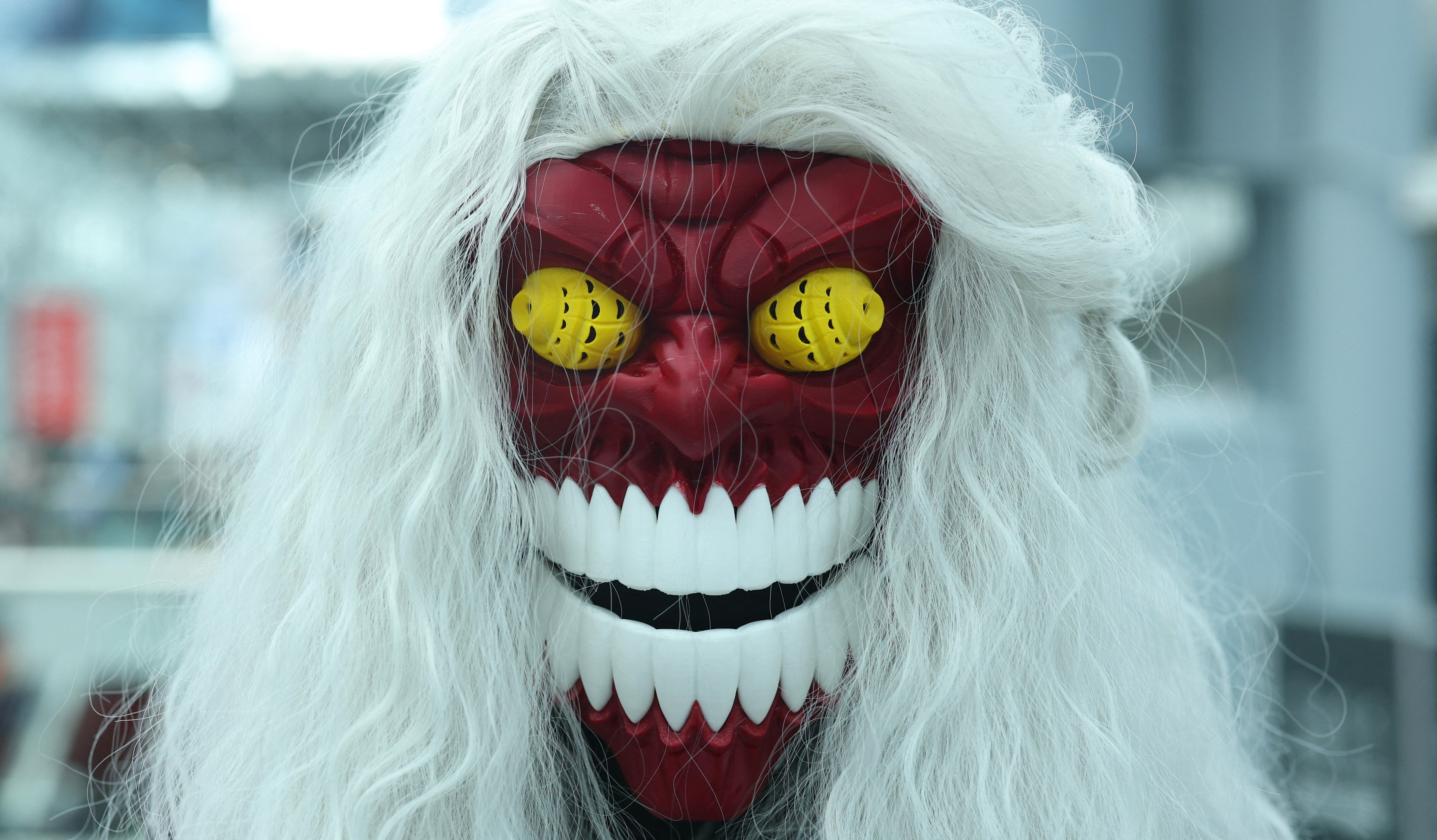 A person wearing a mask with a wide grin, red face, yellow eyes, and long white hair