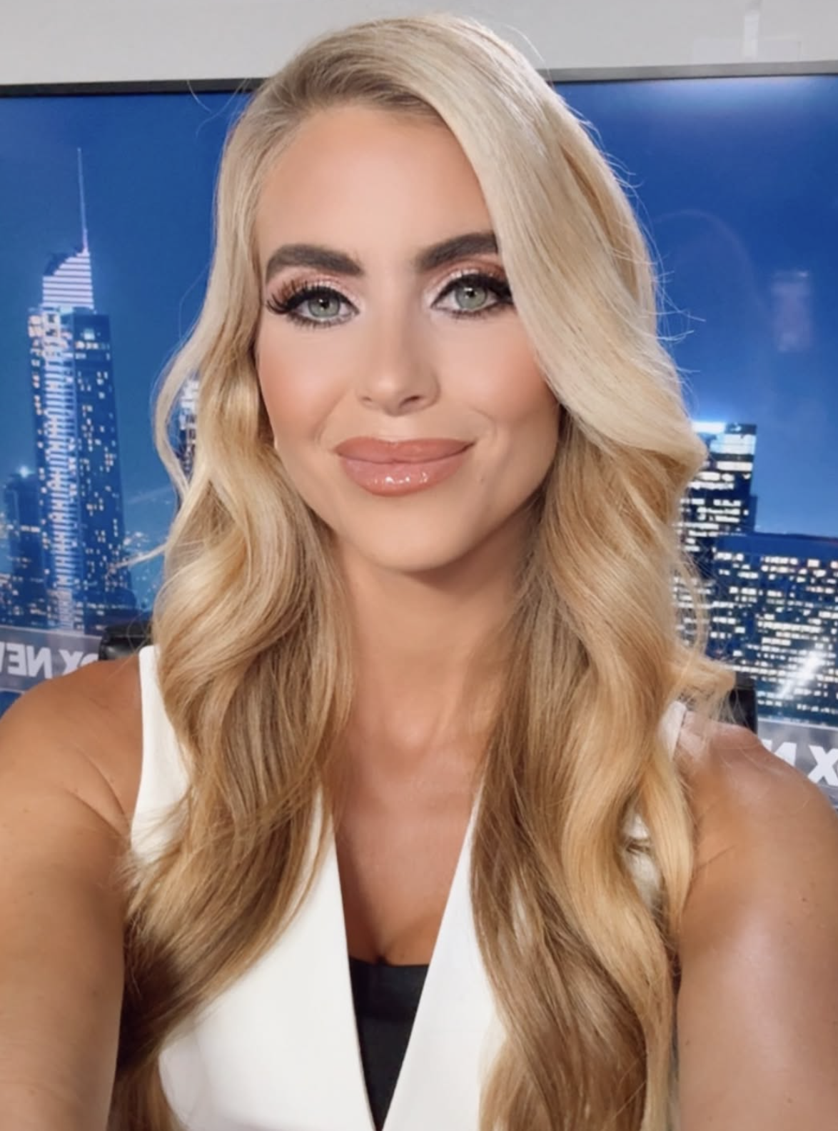 Person with agelong wavy hair, smiling successful beforehand of a cityscape backdrop, wearing a sleeveless top