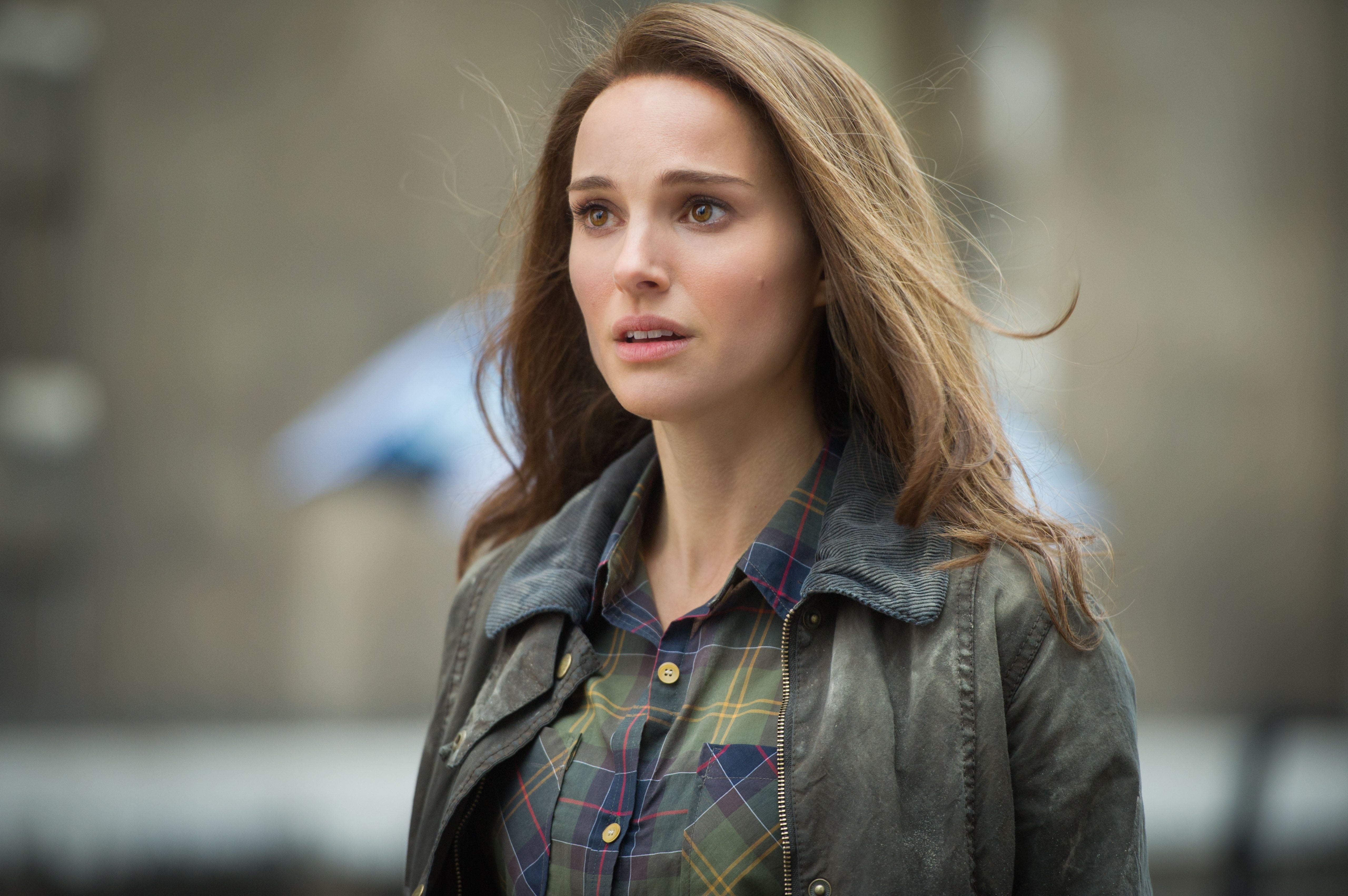 A woman outdoors looks concerned, wearing a plaid shirt under a leather jacket. Urban background is blurred