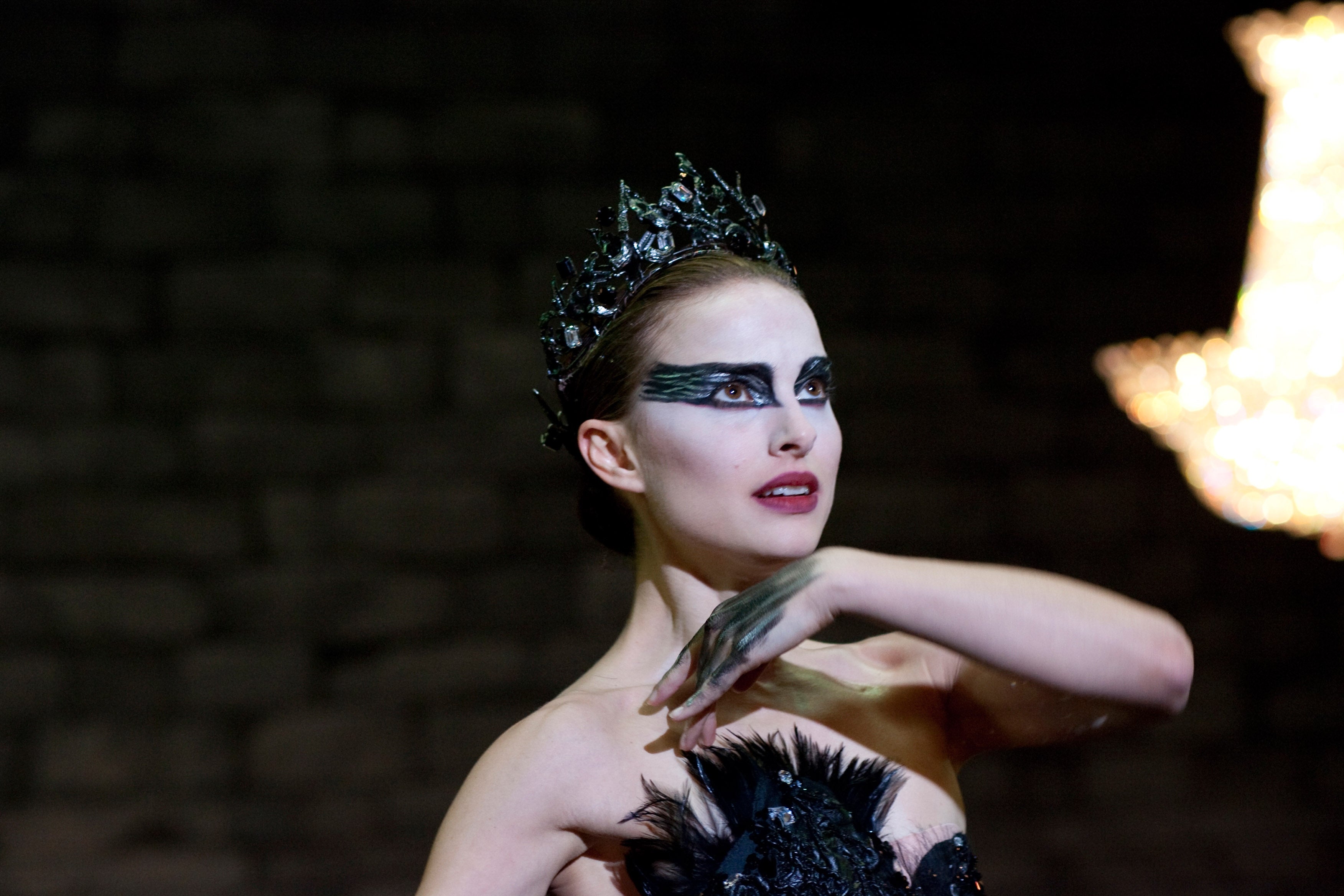 Ballet performer with dramatic feathered makeup and a black crown, striking a poised pose, reminiscent of a scene from a performance