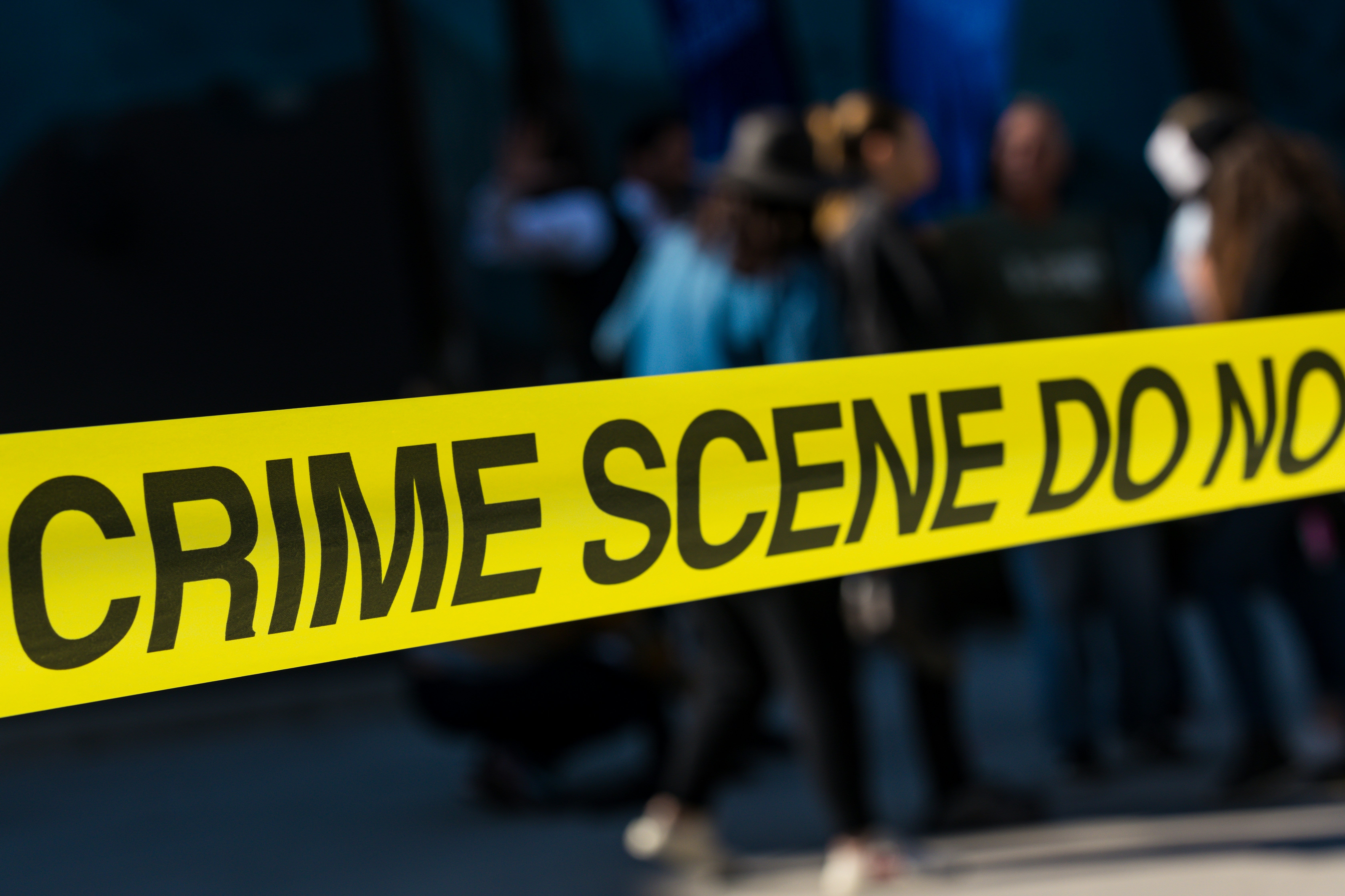 Yellow crime scene tape with "Crime Scene Do Not Cross" in front of blurred figures