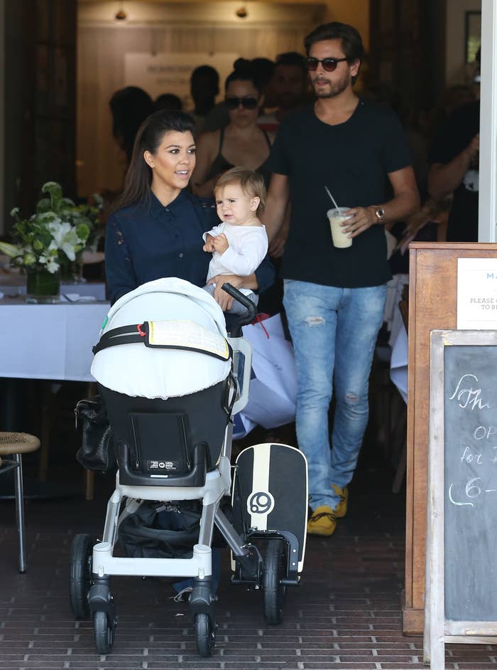 Kourtney pushes a stroller with baby Penelope, with Scott walking behind