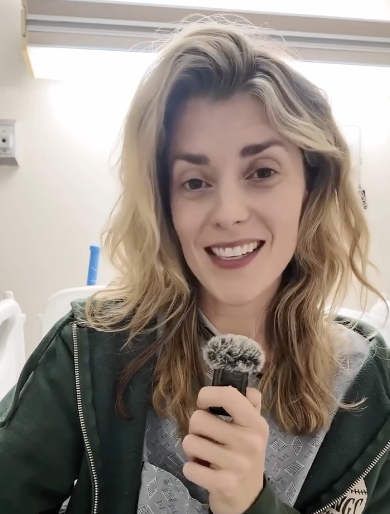 Person smiling, holding a microphone, possibly recording content related to games. Casual attire, appears relaxed and engaging