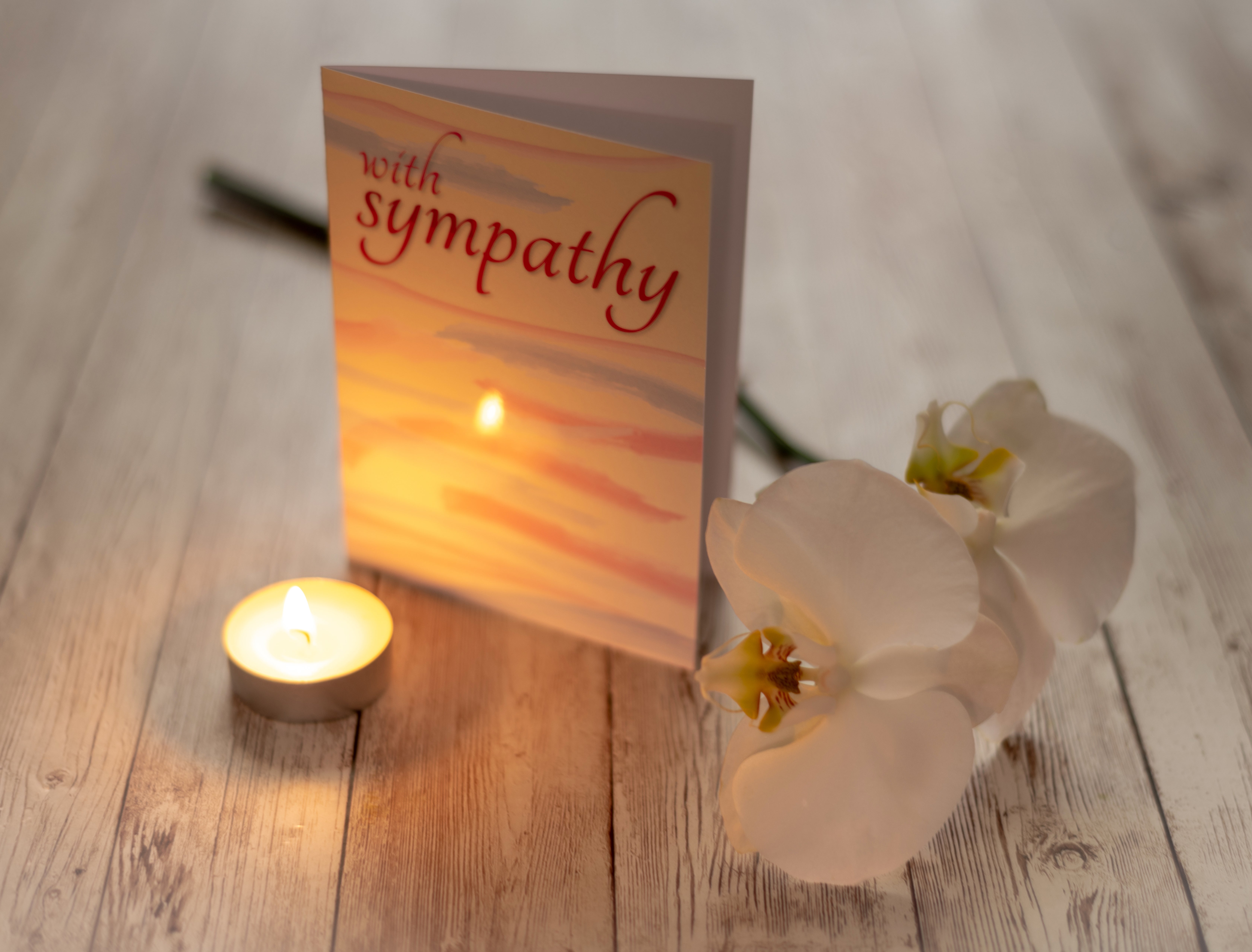 Sympathy card on a table with a lit candle and white orchid, suggesting a somber moment or memorial setting
