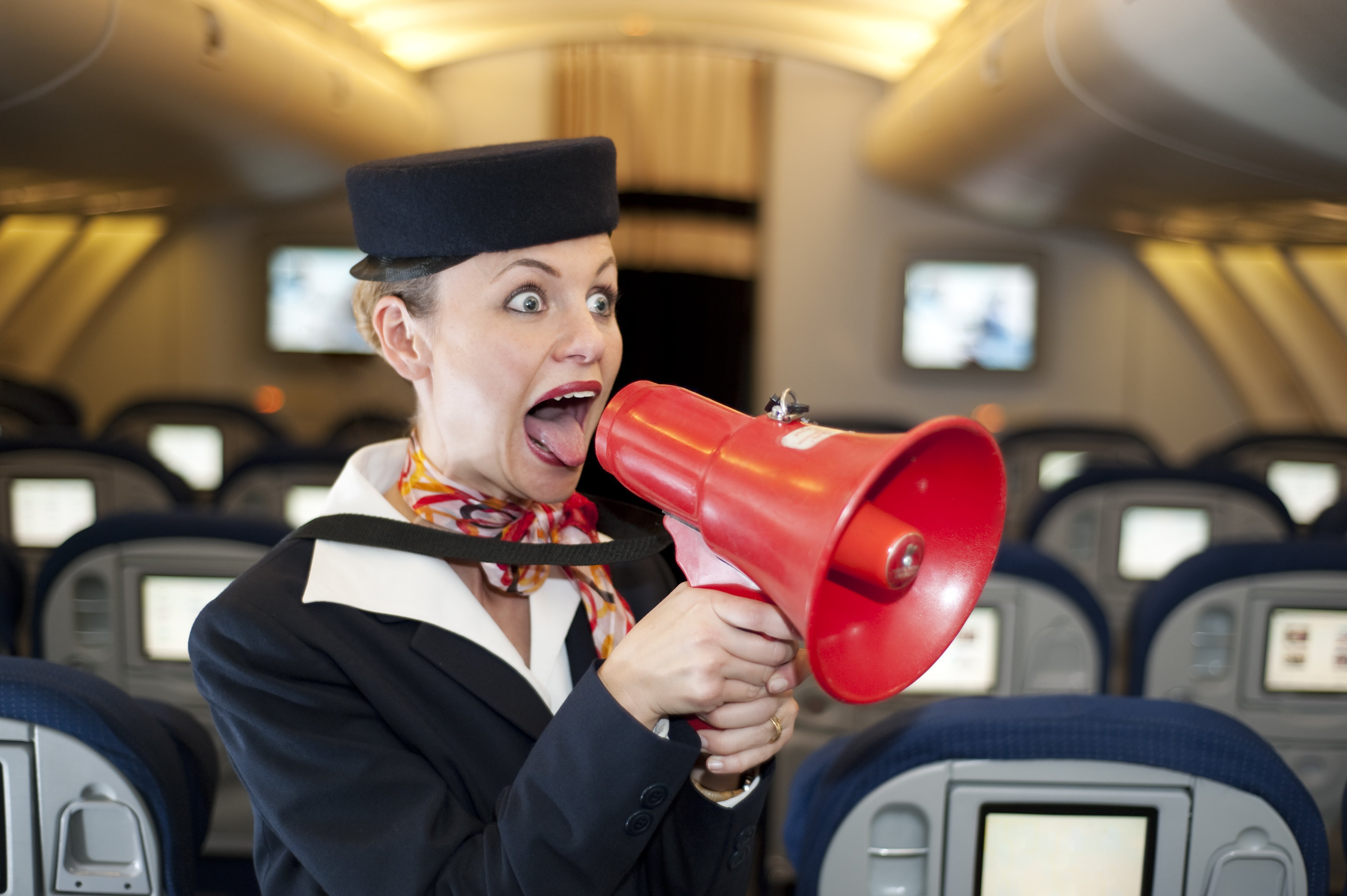 Flight attendant in airline uniform humorously using a red megaphone inside an aircraft cabin