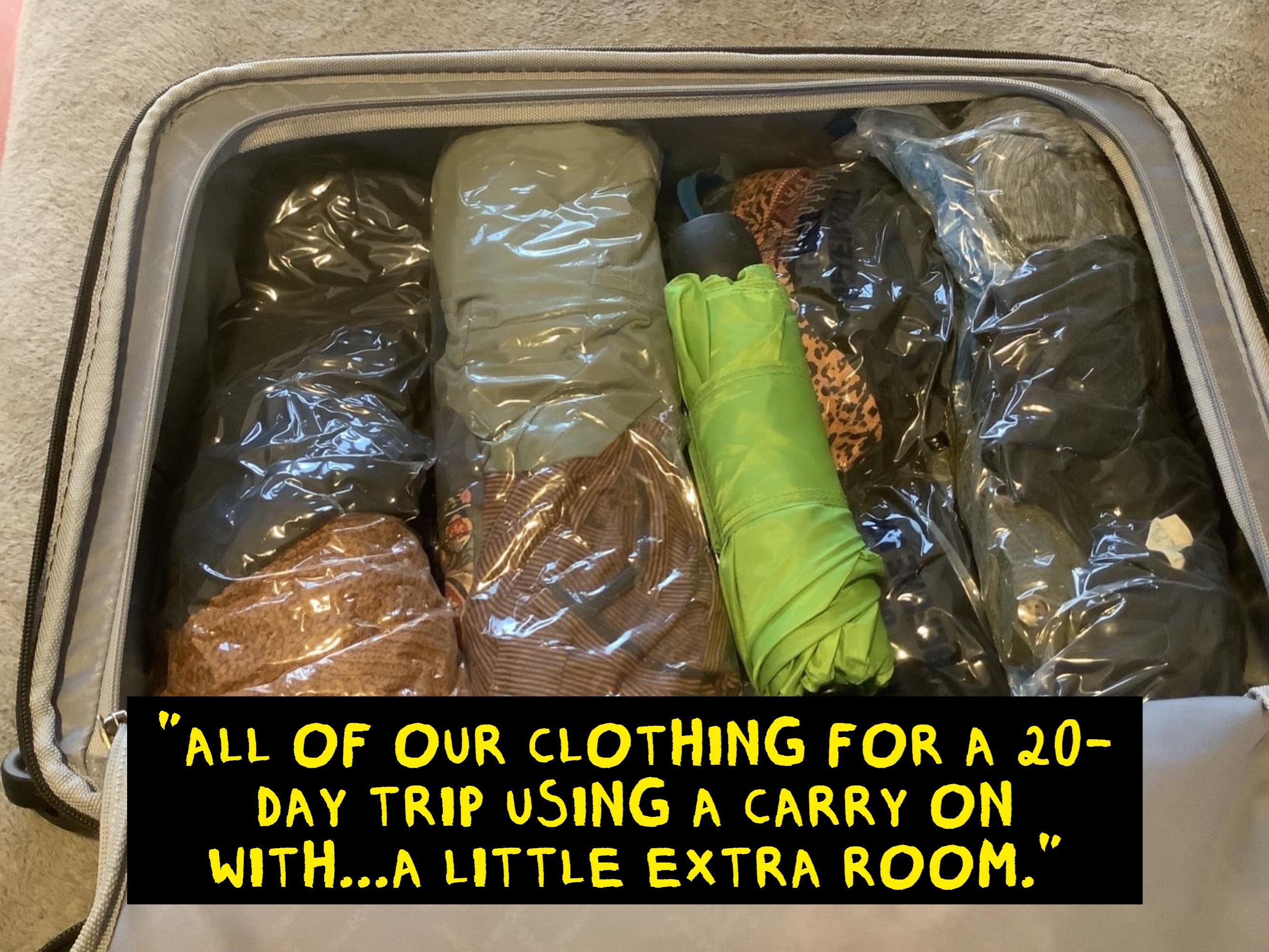 Open suitcase with neatly packed clothing and a green umbrella, organized in clear plastic bags