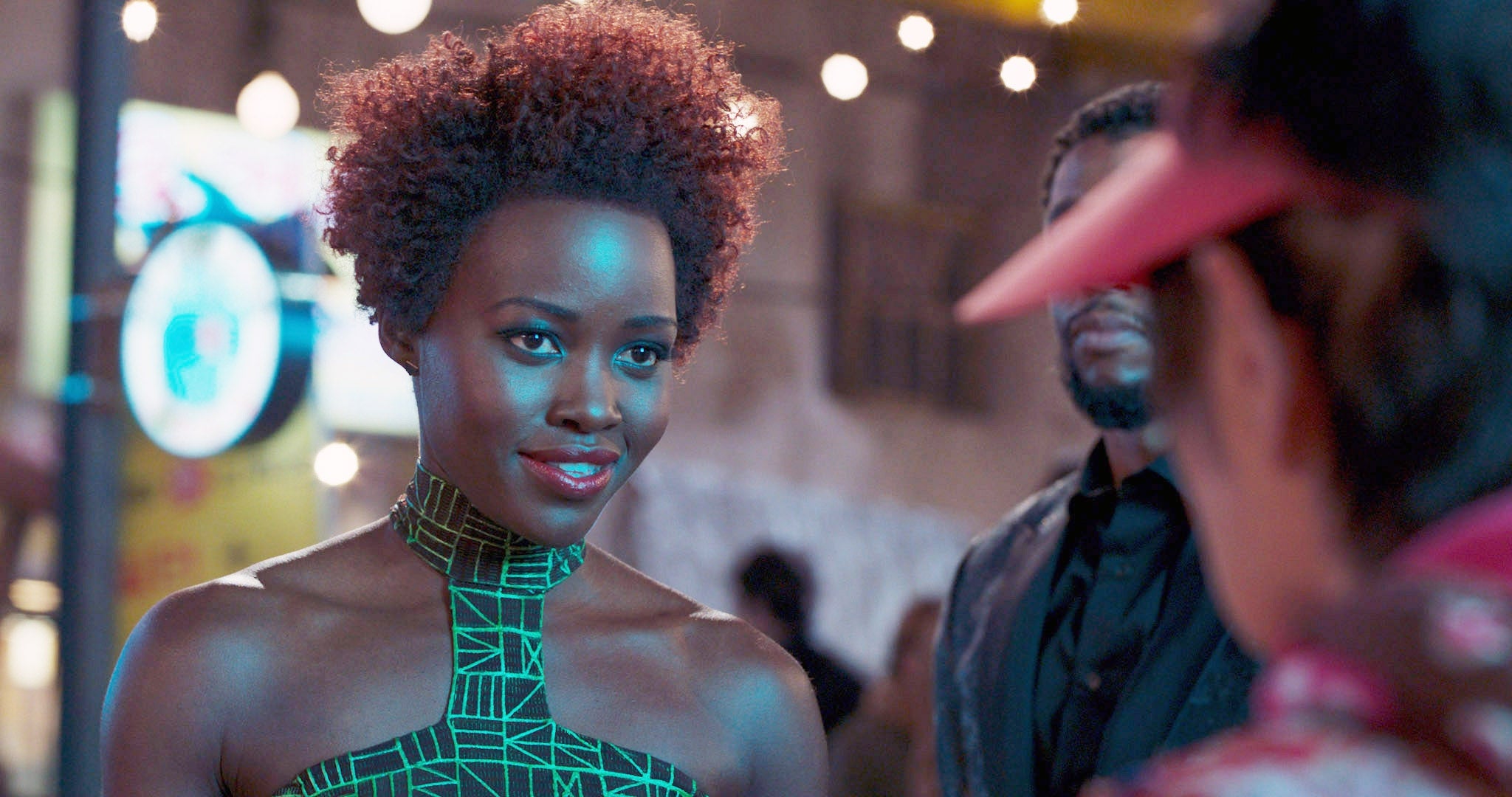 Person in a geometric-patterned dress at a nighttime event, engaging in conversation with others
