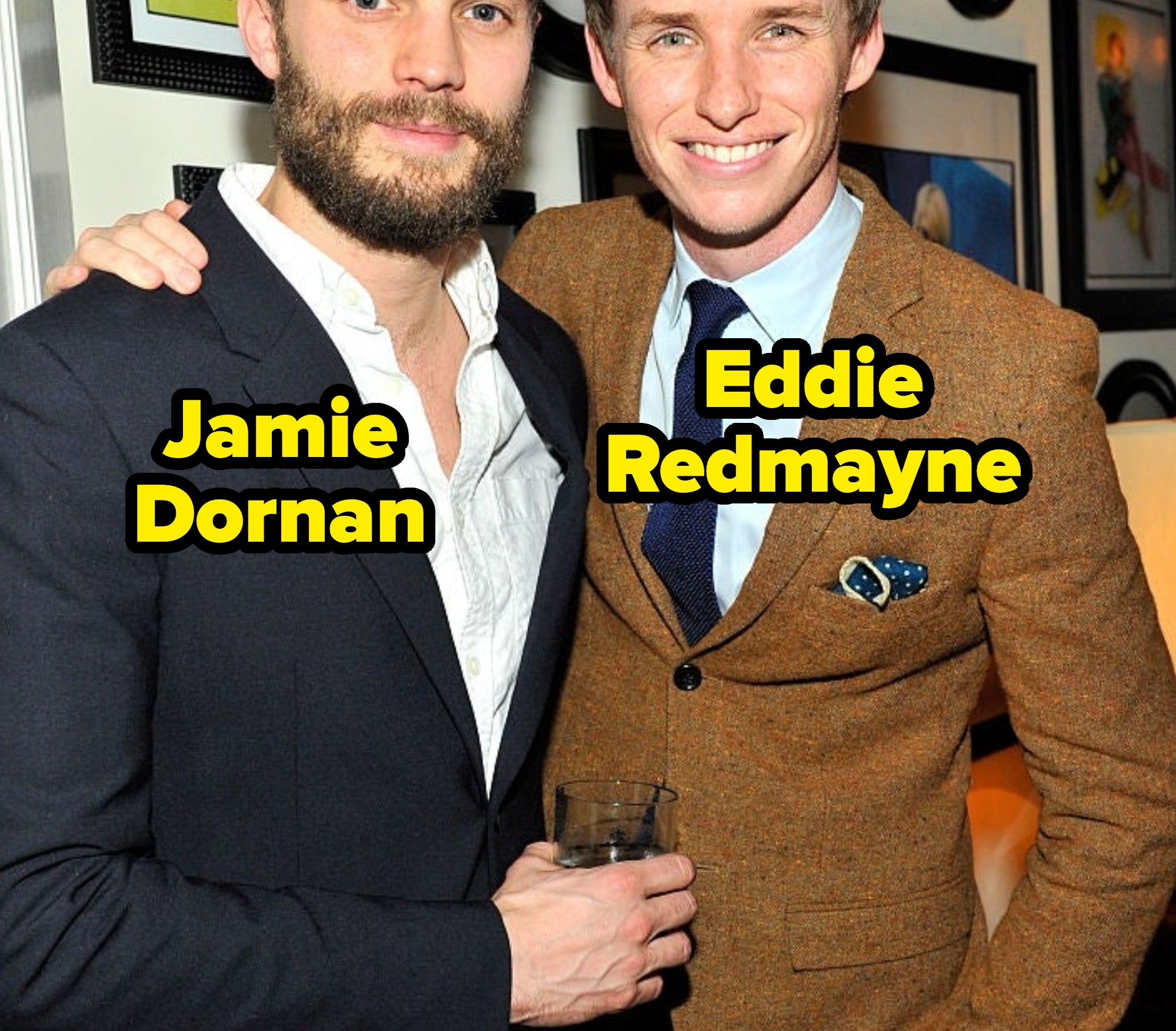 Two men in suits at an event, one with a beard holding a drink, the other in a brown tweed suit with a tie, smiling and posing together