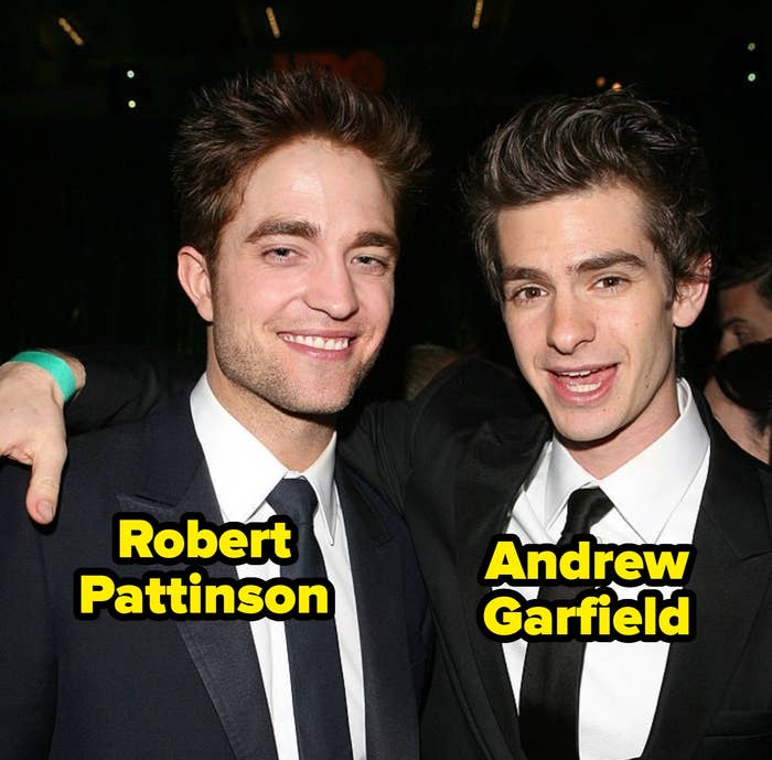 Two men in suits pose together at an event, one with his arm around the other. Both are smiling and dressed in classic formal attire
