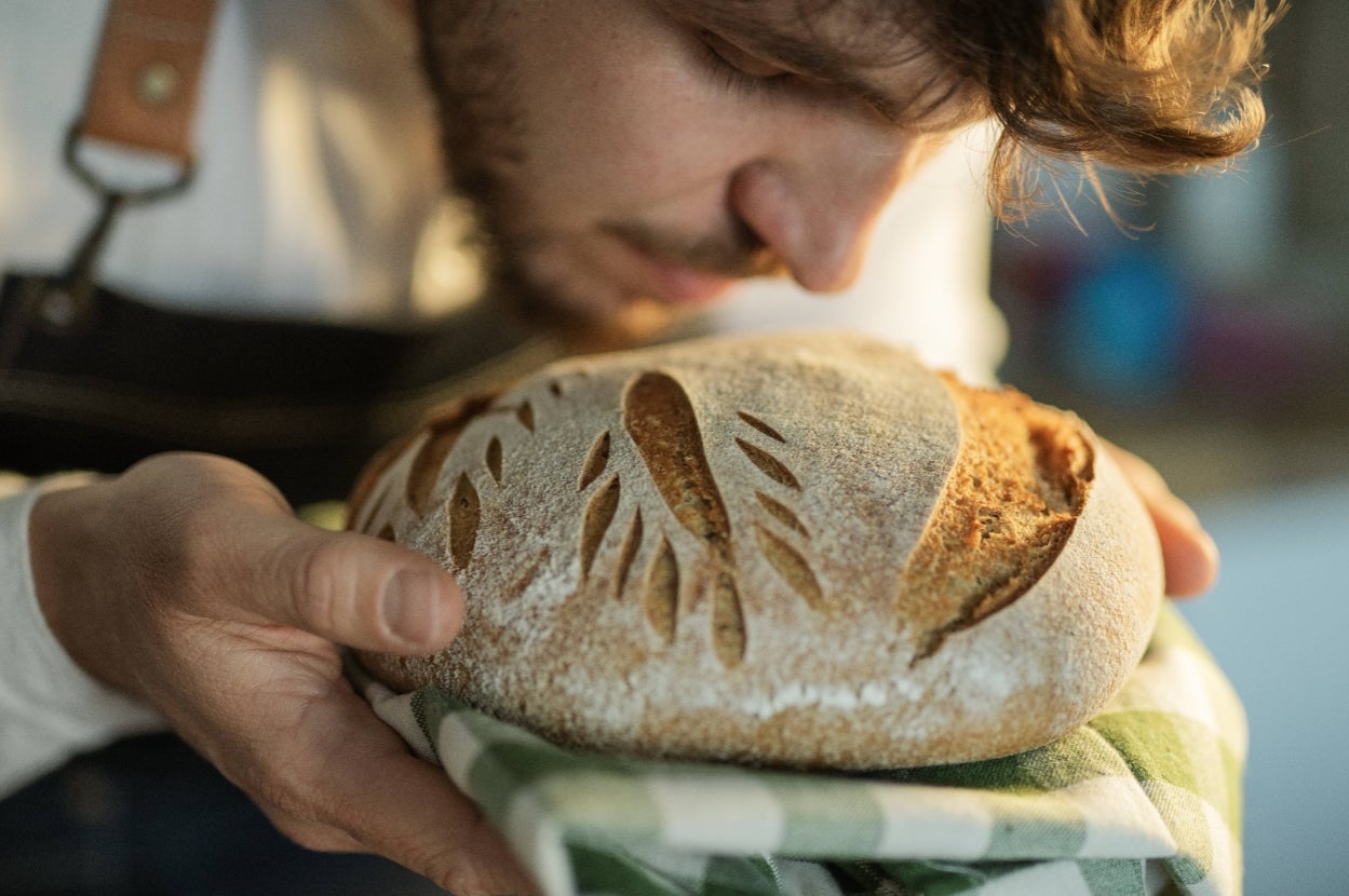 Person holding and smelling a freshly baked artisan bread with a decorative pattern on top