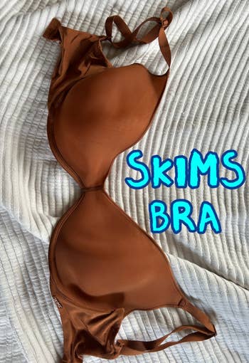 Brown bra with adjustable straps laid connected a textured cloth surface, highlighting its creaseless plan and supportive contour