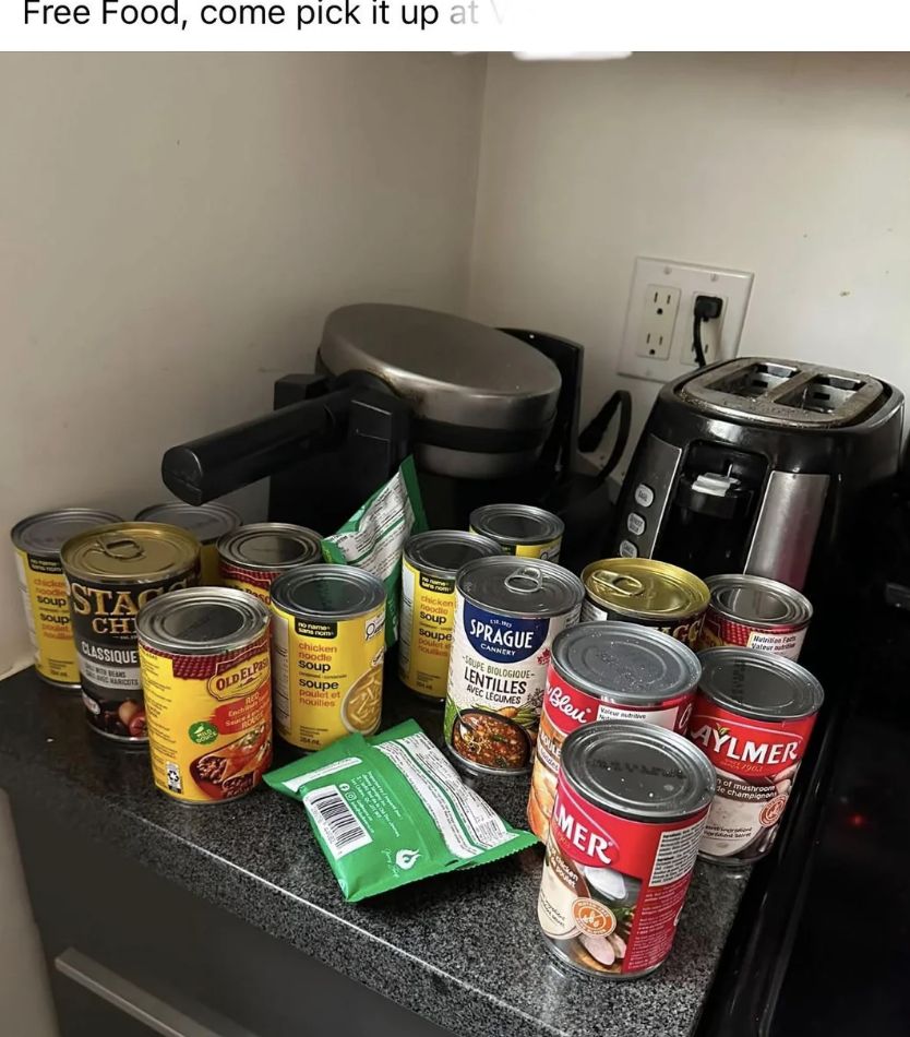 Cans of soup and other canned foods are displayed on a kitchen counter next to a toaster and a kettle