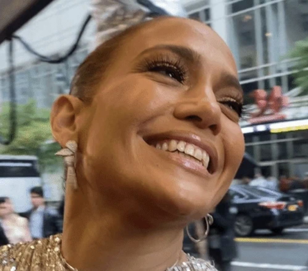 Person smiling with elegant earrings and sequined outfit, outdoors with blurred city background