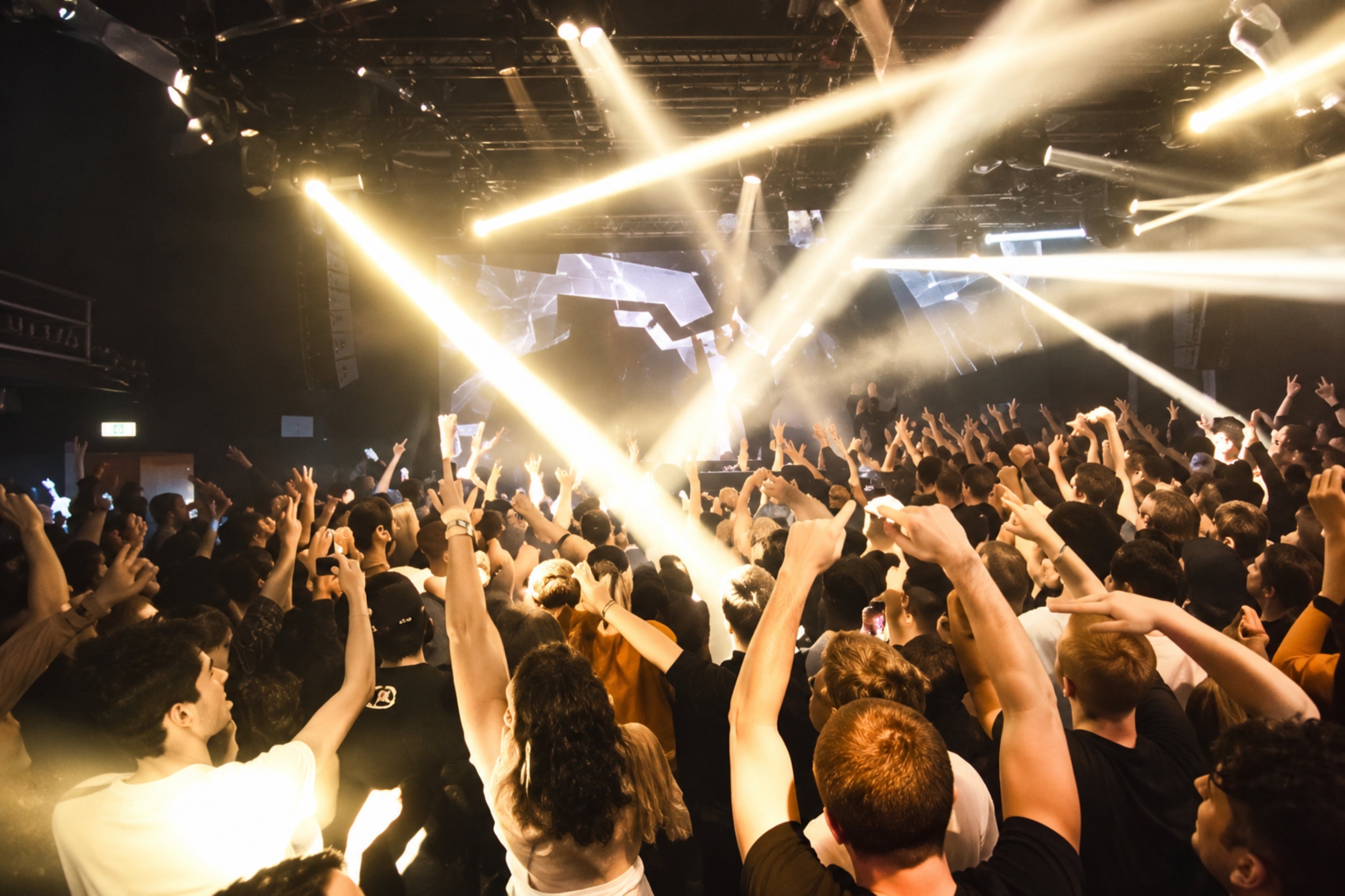 Concert audience with hands raised, bright stage lights illuminating the energetic crowd